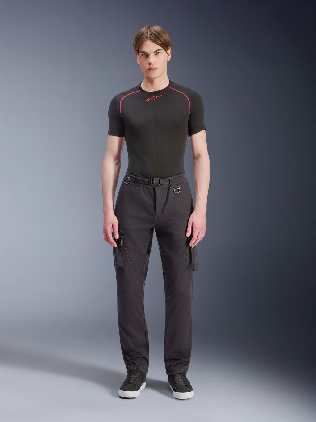 Pantalon Cargo Alpinestars Flex-AST - Court, noir, porté par un mannequin homme avec un t-shirt technique noir et des baskets noires, pantalon de moto urbain doté de multiples poches cargo, d'une coupe fuselée et d'une ceinture intégrée avec boucle et anneau en D