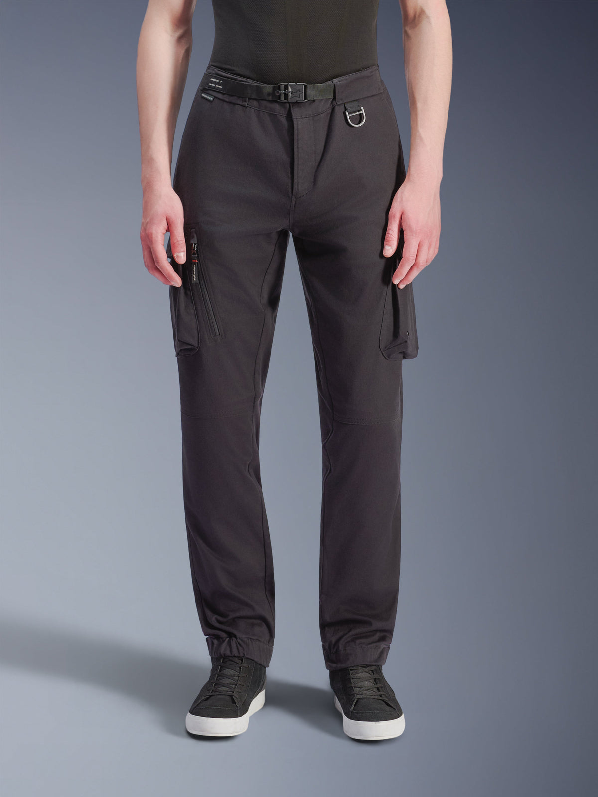 Alpinestars Flex-AST Cargo Pants - Short, pantalon de moto urbain noir, vue de face avec tissu technique extensible, plusieurs poches cargo avec détails zippés latéraux, passant de ceinture avec anneau en D métallique, coupe fuselée avec ourlets élastiqués, porté avec des baskets noires