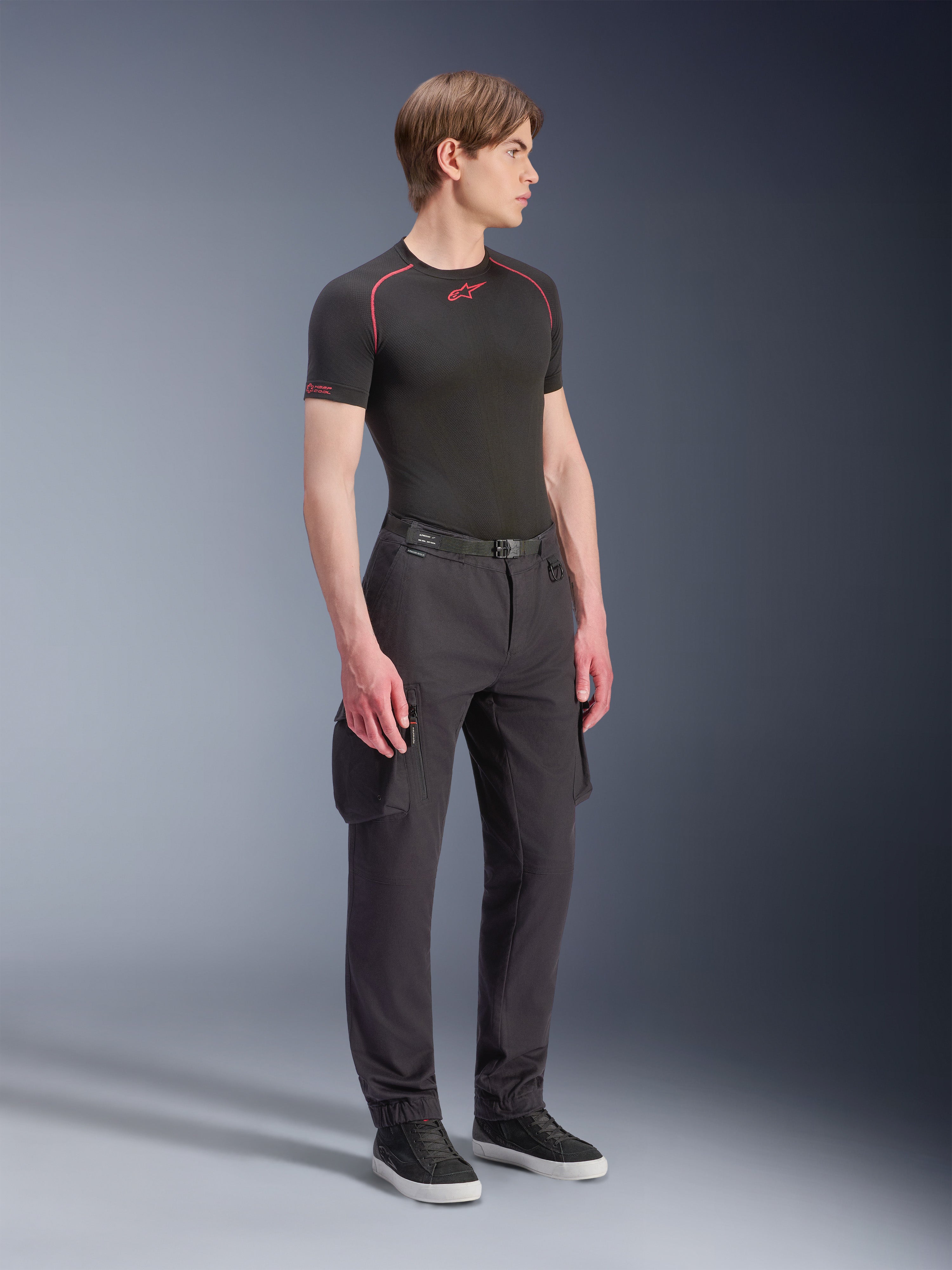 Pantalon Cargo Alpinestars Flex-AST, noir, pantalon de moto urbain avec poches cargo et ourlets élastiqués, porté par un mannequin avec une sous-couche noire à manches courtes et des baskets, coupe fuselée moderne