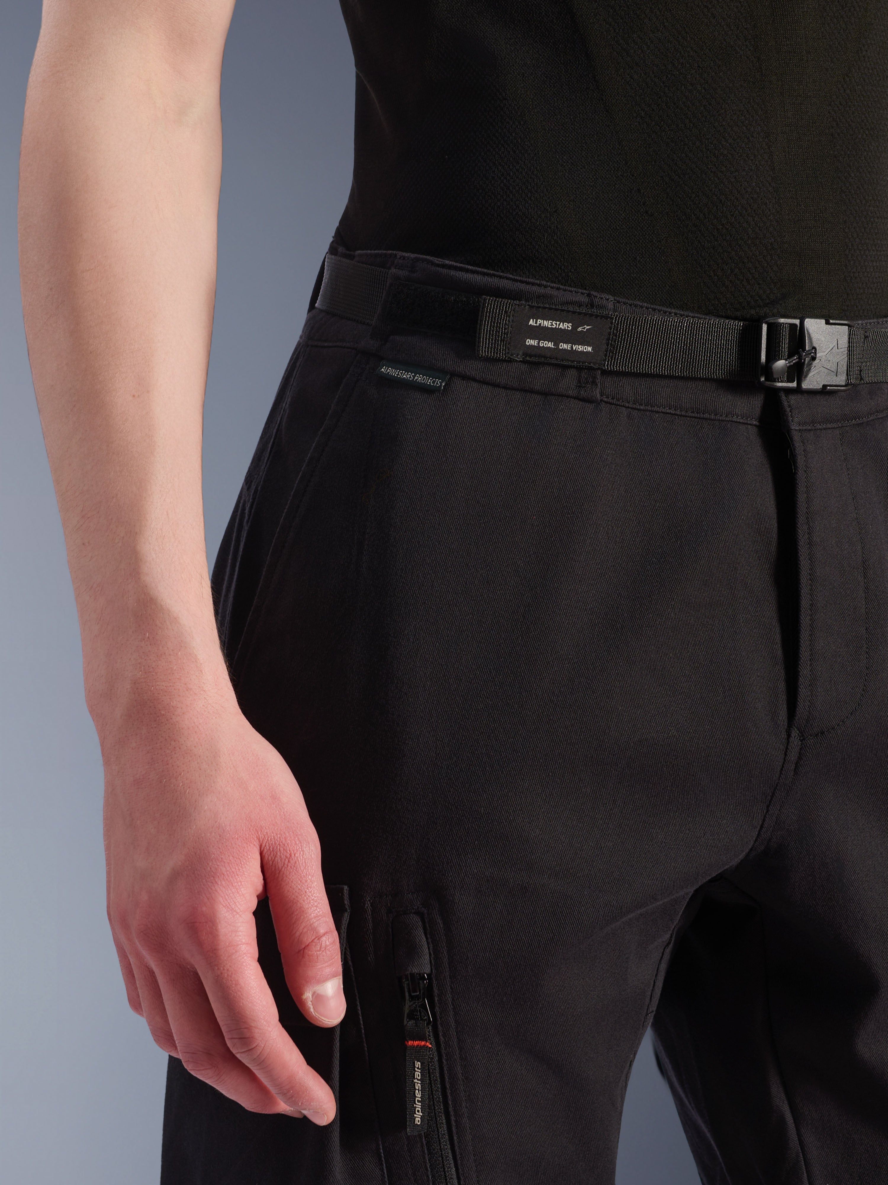 Pantalon Cargo Alpinestars Flex-AST, noir, gros plan sur la zone de la taille et des hanches, doté d'une ceinture réglable intégrée avec marquage Alpinestars, fermeture par boucle et poche cargo zippée, tissu technique extensible pour équipement moto urbain