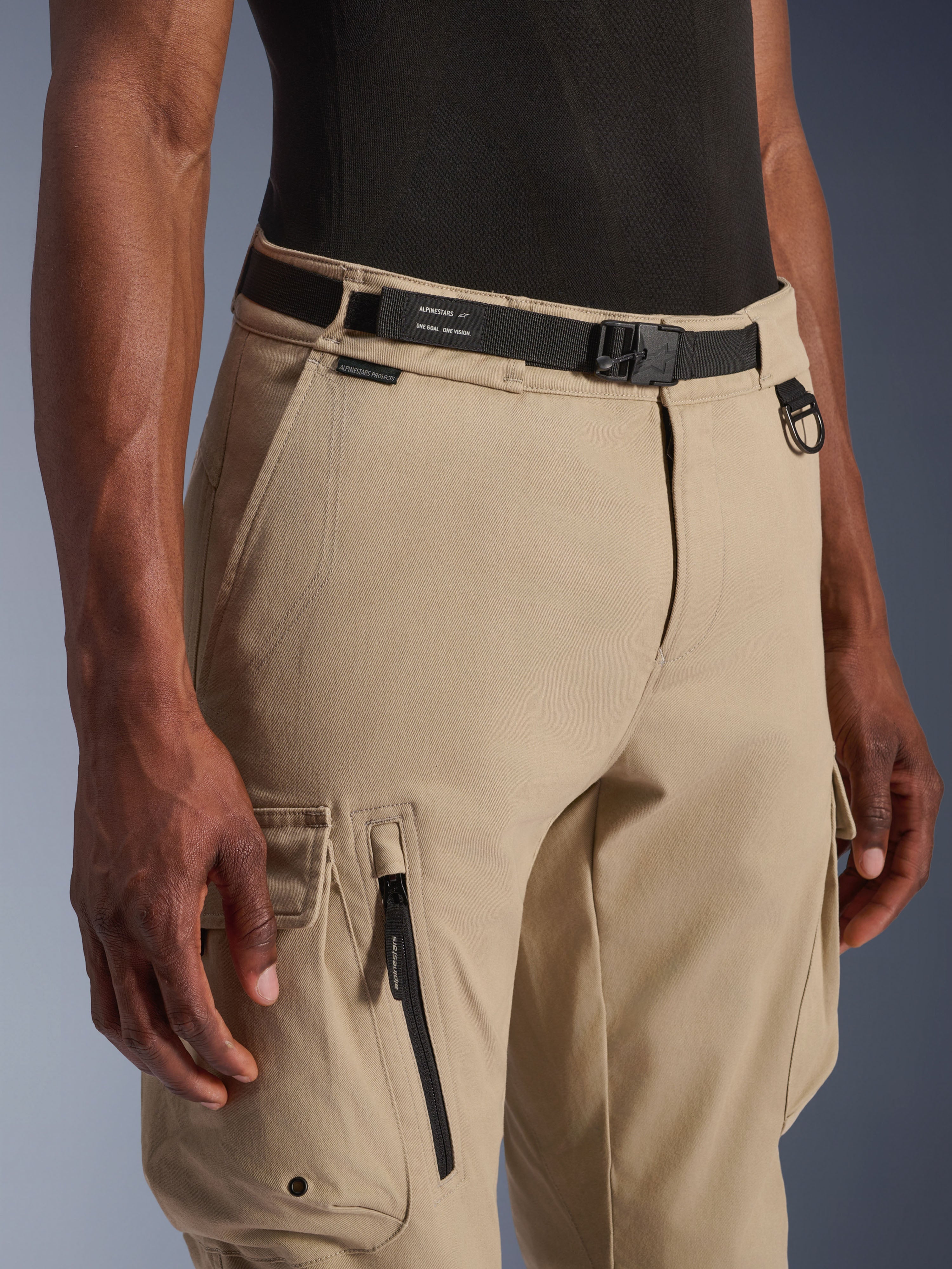 Alpinestars Flex-AST Cargo Pants - Short, Light Beige, close-up view of waist and thigh, featuring a black adjustable belt with Alpinestars branding, metal D-ring, and functional cargo pockets with zippers and snap flaps, urban contemporary motorcycle gear