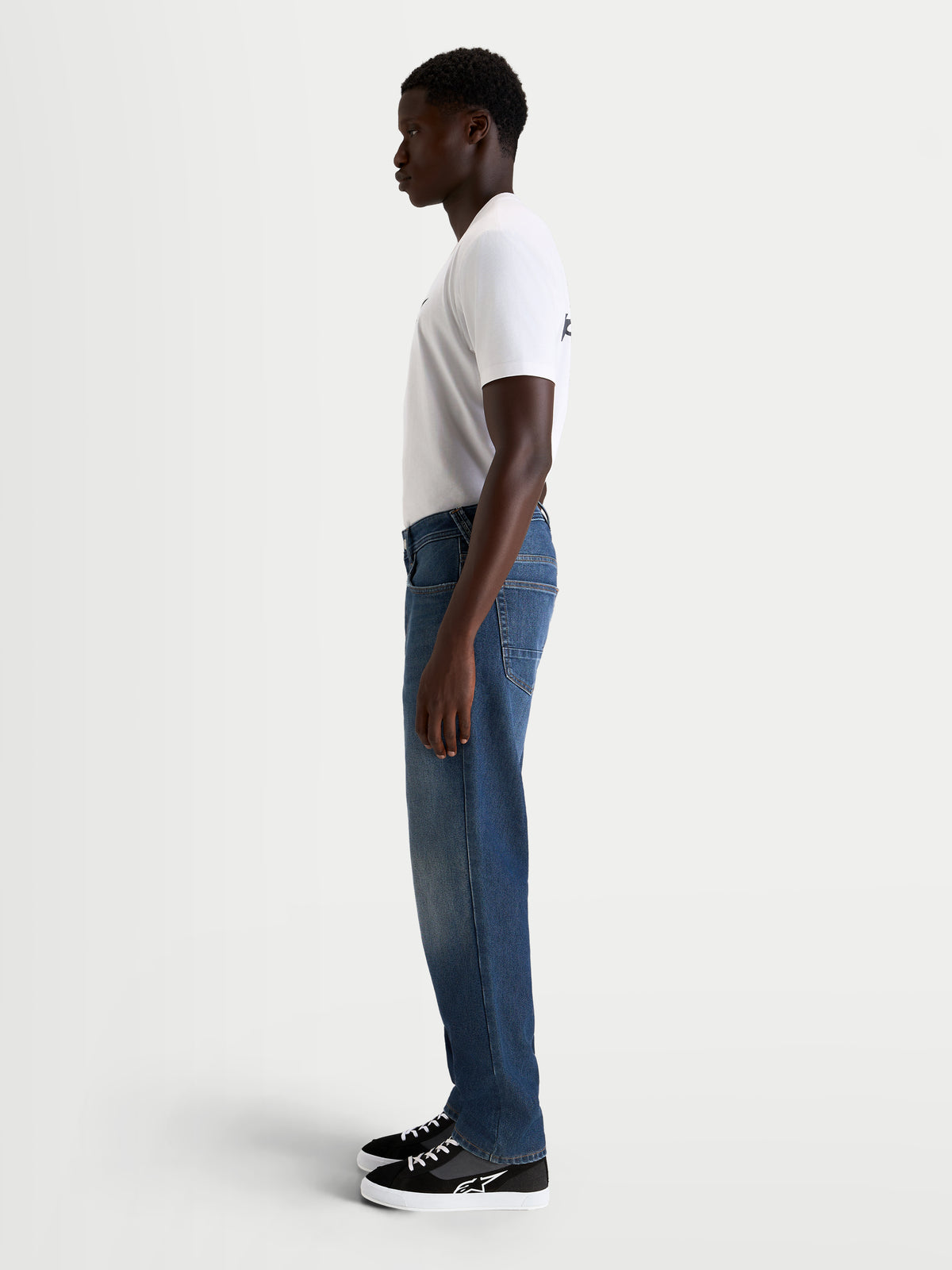 Alpinestars Flex-AST 8 Denim Pants, men's urban motorcycle riding jeans in medium blue, side profile view on a model wearing a white t-shirt and casual riding shoes, AA-rated single-layer denim with stretch construction
