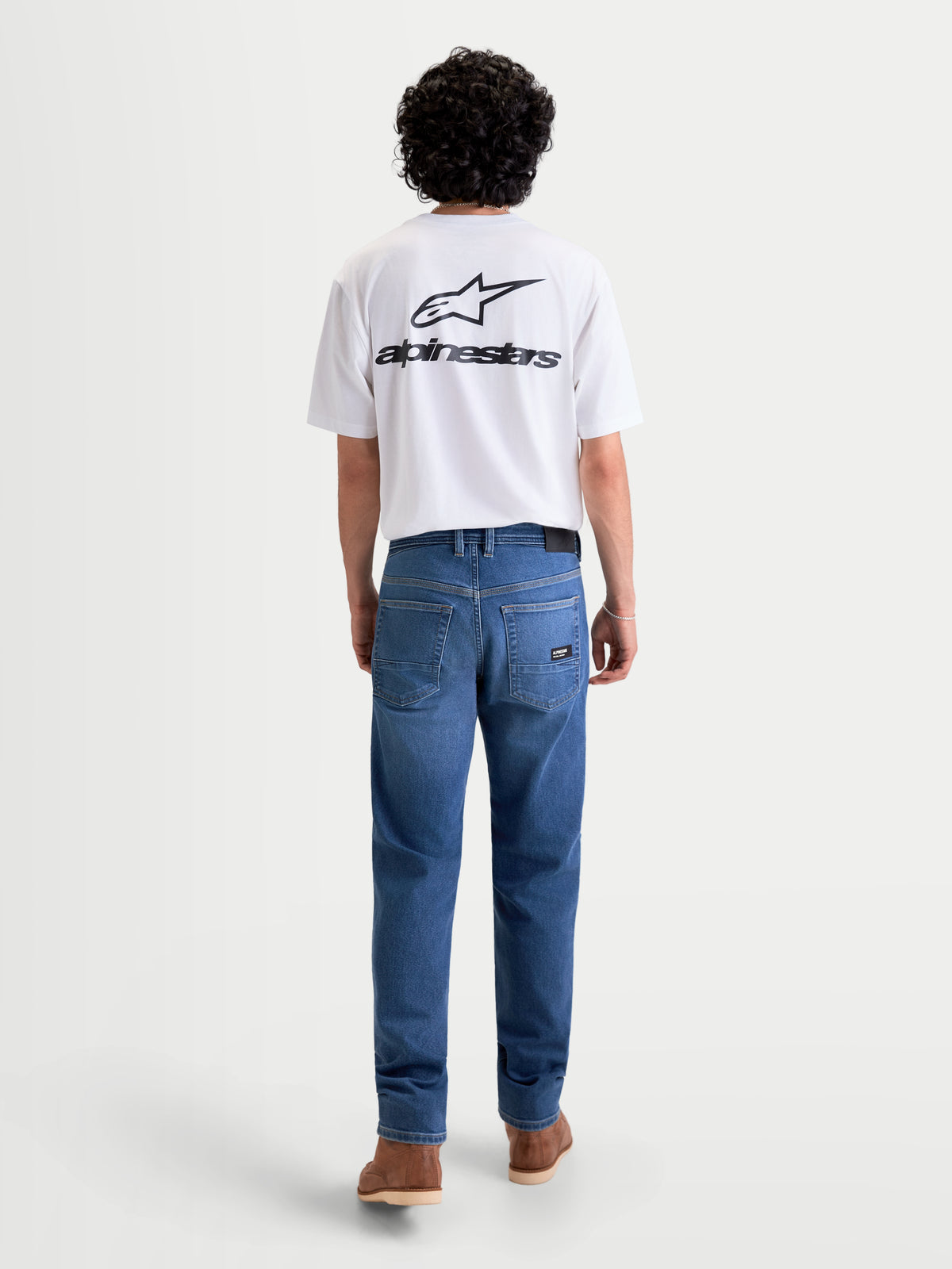 Alpinestars Flex Ast 7 Denim Pantalons, pantalon de moto urbain pour homme en bleu clair, vue de dos sur un modèle portant un t-shirt blanc, mettant en valeur le denim technique monocouche et la disposition à cinq poches