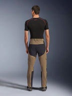 Pantalon Alpinestars Flex-AST Explorer, Walnut Black, vue arrière sur modèle, avec assise renforcée noire et textile extensible marron, associé à une couche de base noire et des bottes de moto techniques, équipement de moto d'aventure robuste