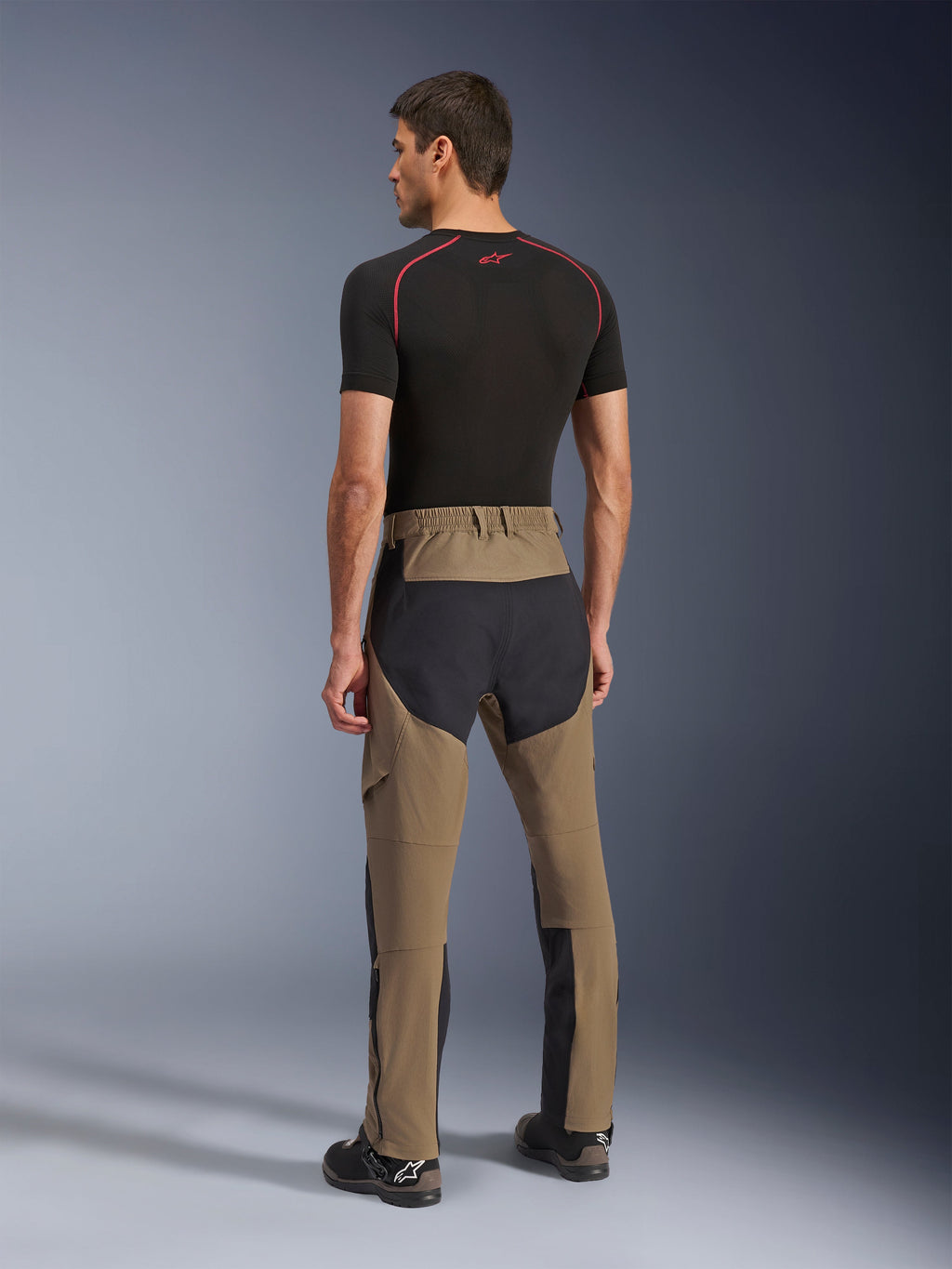 Pantalon Alpinestars Flex-AST Explorer, pantalon de moto d'aventure, Walnut Black, vue arrière sur modèle montrant les panneaux d'assise et de jambes en ripstop noir, construction en textile extensible et longues fermetures éclair au bas des jambes pour le tourisme d'aventure
