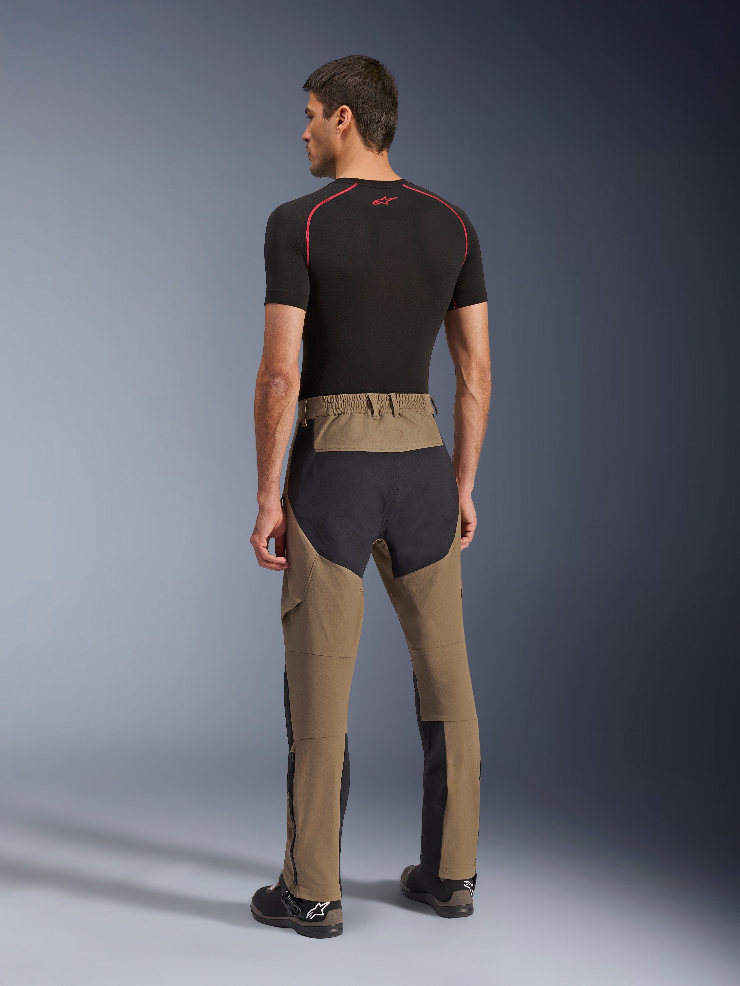 Pantalon Alpinestars Flex-AST Explorer, pantalon de moto d'aventure, Walnut Black, vue arrière sur modèle montrant les panneaux d'assise et de jambes en ripstop noir, construction en textile extensible et longues fermetures éclair au bas des jambes pour le tourisme d'aventure
