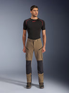 Pantalon Alpinestars Flex-AST Explorer, pantalon de moto touring, marron noyer et noir, avec panneaux de genoux renforcés et poches zippées sur les cuisses, porté avec une couche de base noire à manches courtes, vue en pied