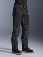 Pantalon Alpinestars C-1 Air, pantalon de moto urbain, noir, doté de panneaux en maille technique respirante et d'une construction en polyfibre, porté avec des baskets noires, design épuré et fonctionnel pour la conduite en ville.