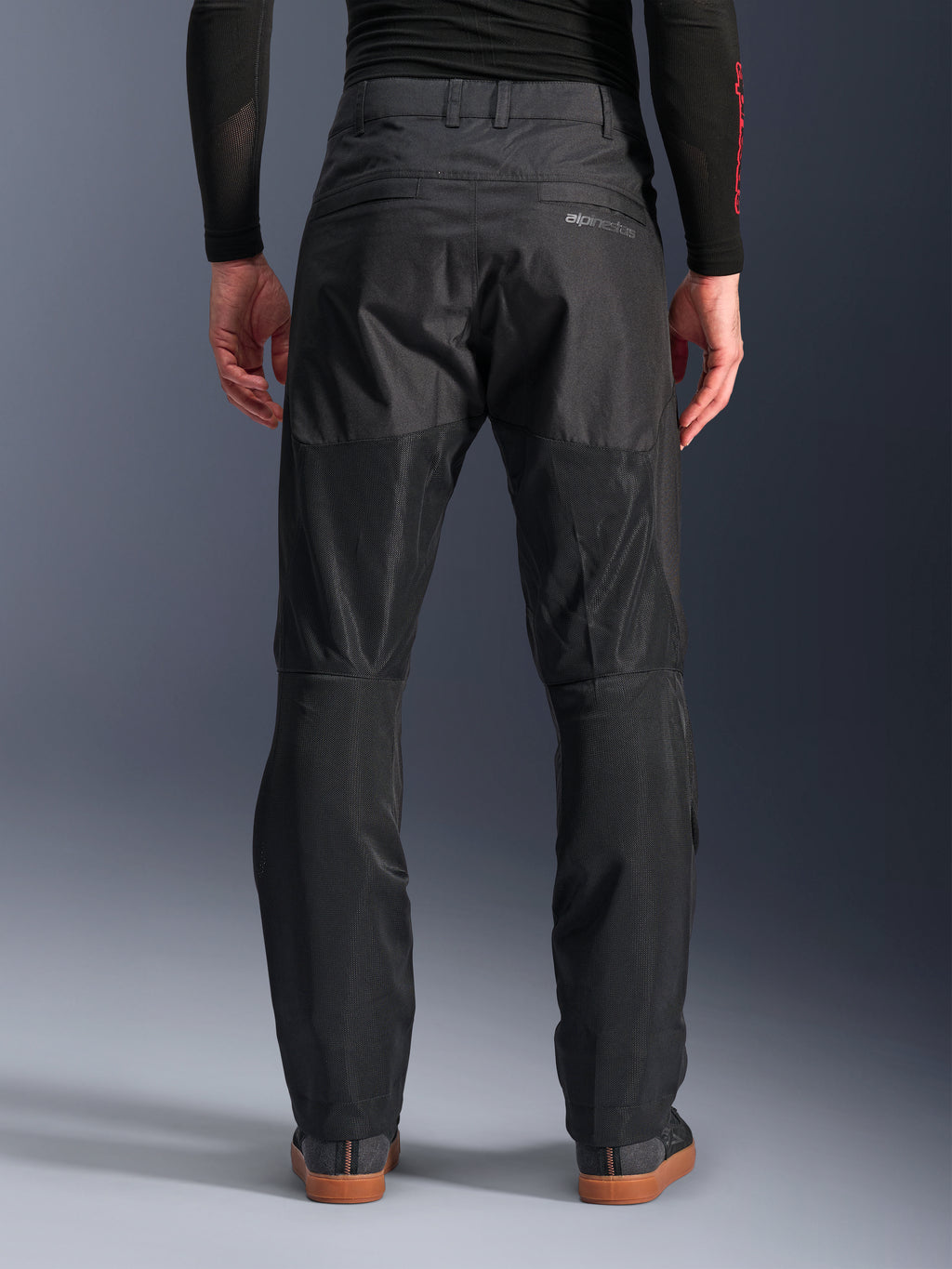 Alpinestars C-1 Air Pants, vue arrière, noir, pantalon de moto urbain en textile doté de larges panneaux en mesh technique à l'arrière des jambes pour la ventilation, design épuré avec logo discret, porté avec une couche de base noire et des chaussures de moto décontractées.