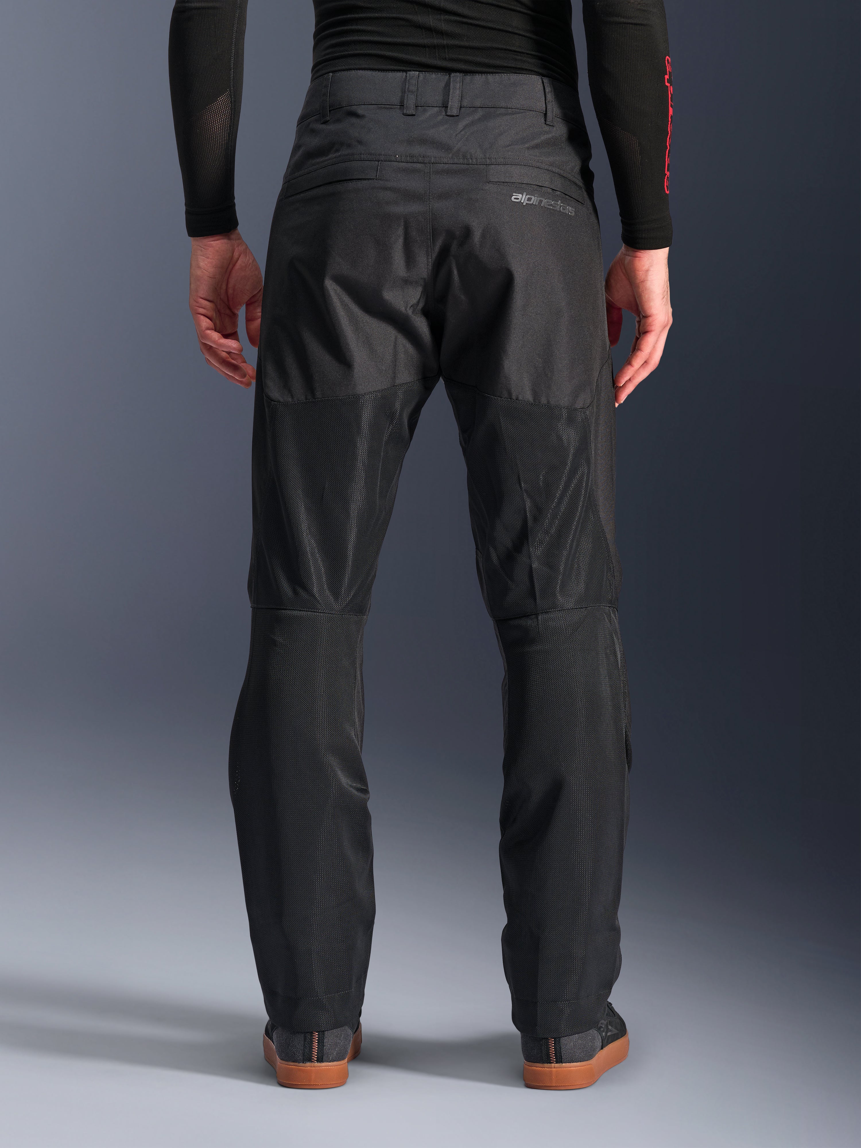 Alpinestars C-1 Air Pants, vue arrière, noir, pantalon de moto urbain en textile doté de larges panneaux en mesh technique à l'arrière des jambes pour la ventilation, design épuré avec logo discret, porté avec une couche de base noire et des chaussures de moto décontractées.