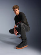 Alpinestars C-1 Air Pants, pantalon de moto urbain, noir, modèle accroupi dans un studio, porté avec un haut noir à manches longues et des baskets noires à semelles marron, doté de panneaux en mesh respirant et d'un style urbain contemporain