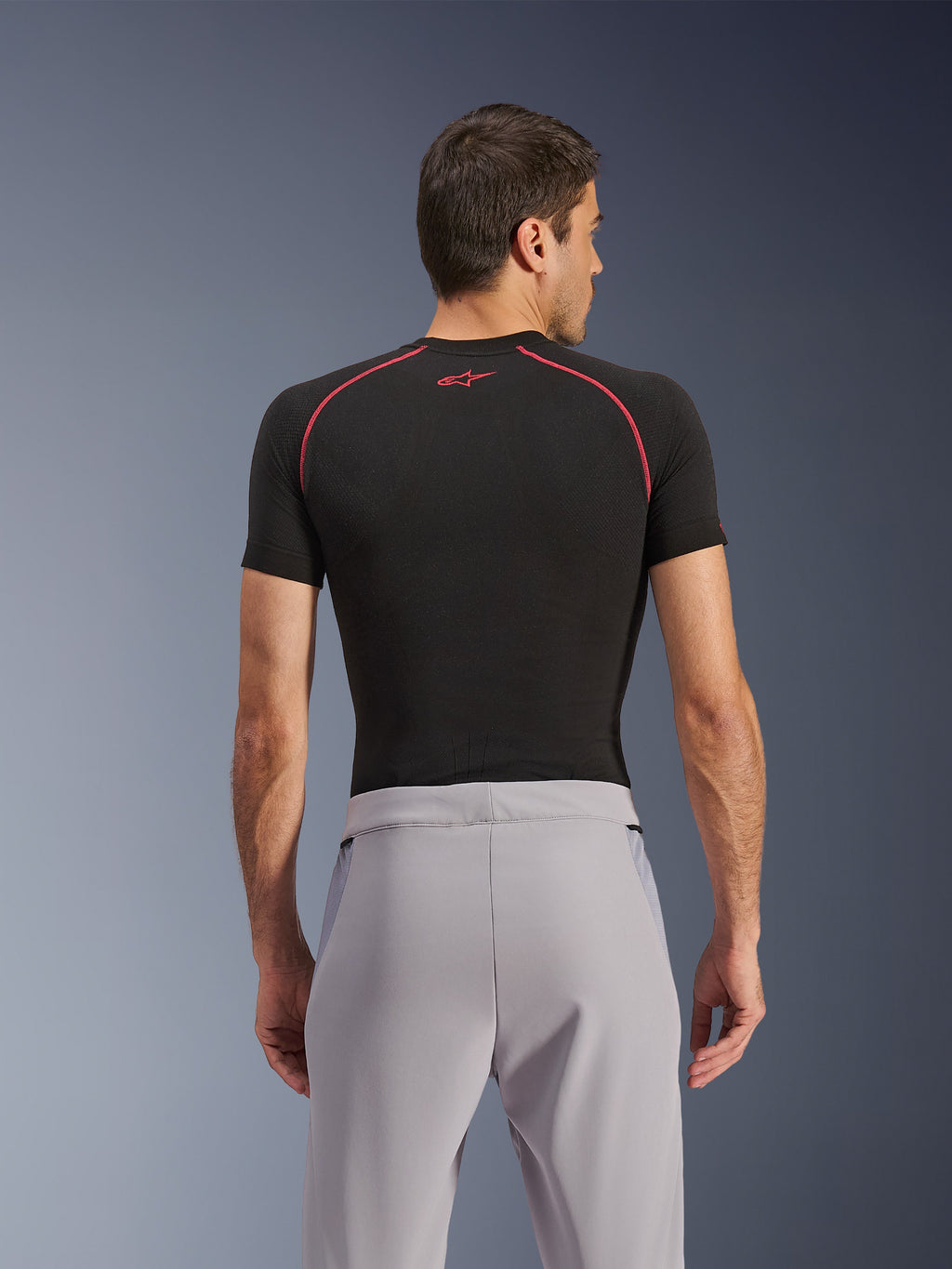 Pantalon Alpinestars Aeroshell Airflow, Gris Moyen, vue de dos, porté avec un vêtement de corps noir à manches courtes avec coutures et logo rouges, doté d'un textile softshell extensible léger et de panneaux en maille pour une ventilation maximale, coupe sport ergonomique pour la conduite à moto