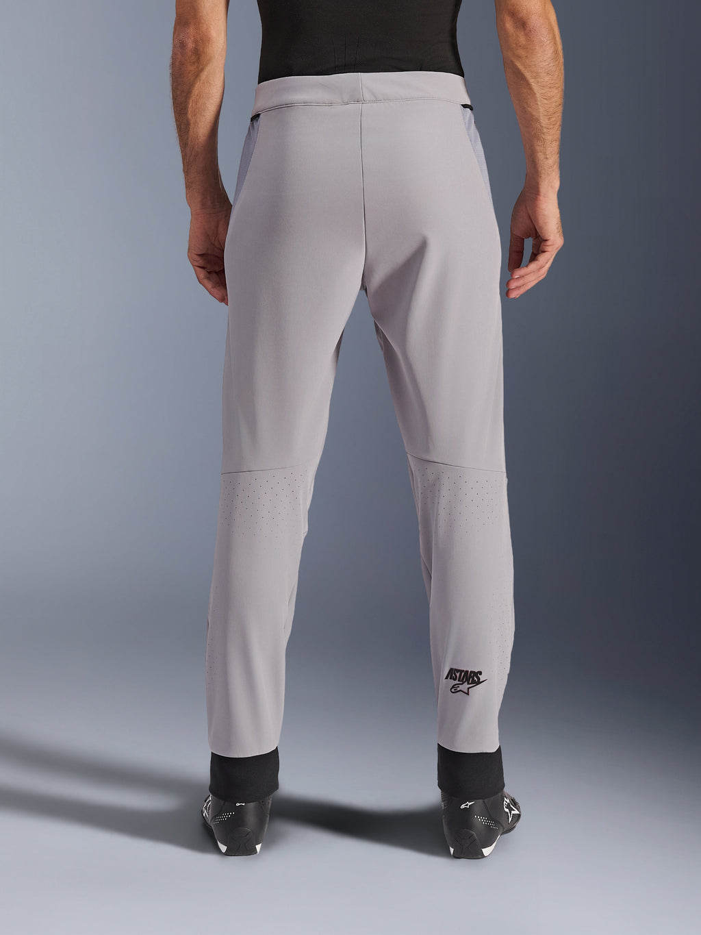 Pantalon Alpinestars Aeroshell Airflow, pantalon de moto, gris moyen, vue arrière montrant les zones perforées au laser sur les mollets et le logo Astars noir, construction en textile softshell avec poignets de cheville noirs et panneaux de hanche en maille.
