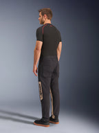 Pantalon Alpinestars Flex-AST Canvas, Black Aluminum, pantalon de moto urbain, avec empiècements latéraux beiges et marquage Alpinestars, porté avec une couche de base noire et des baskets, vue arrière montrant un style inspiré du workwear et une coupe moto ergonomique.