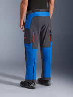Pantalon Alpinestars Maxdura Dual, bleu royal et gris foncé, vue arrière montrant les poches zippées et les zones de ventilation, coupe par-dessus la botte avec des bottes Alpinestars noires, équipement robuste pour l'aventure et le dual-sport