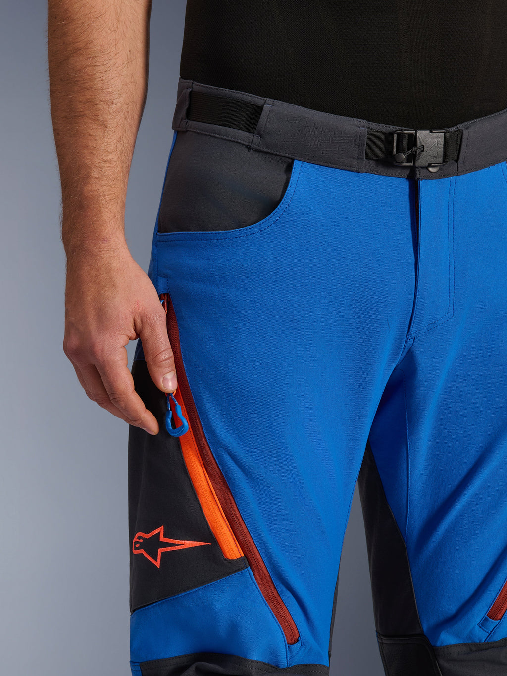 Pantalon Alpinestars Maxdura Dual en Bleu Royal et Gris Foncé, vue rapprochée de la taille avec boucle magnétique, poche cargo zippée avec détails orange et logo Alpinestars rouge, équipement technique de moto d'aventure