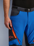 Pantalon Alpinestars Maxdura Dual en Bleu Royal et Gris Foncé, vue rapprochée de la taille avec boucle magnétique, poche cargo zippée avec détails orange et logo Alpinestars rouge, équipement technique de moto d'aventure