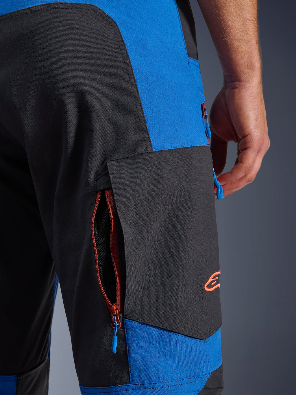 Pantalon Alpinestars Maxdura Dual, bleu royal et gris foncé, gros plan sur la poche cargo latérale zippée, tirettes de zip bleues, logo brodé orange, équipement de moto d'aventure