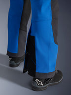 Pantalon Alpinestars Maxdura Dual, bleu royal et gris foncé, gros plan du bas de jambe ajustable avec boutons-pression et soufflet, coupe aventure par-dessus la botte, porté avec des bottes de moto Alpinestars noires