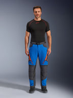 Alpinestars Maxdura Dual Pants, pantalon de moto d'aventure, bleu royal et gris foncé, accents de fermetures éclair orange, porté avec une couche de base Alpinestars noire et des bottes noires, doté de panneaux de genoux renforcés et d'un design technique tout-terrain