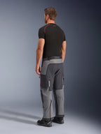 Alpinestars Maxdura Dual Pants, Adventure Motorcycle Pants, Dark Gray and Deep Gray, worn by a model from a back-side view, featuring red accents on zippers and logo, reinforced gray panels, cargo pockets, and over-the-boot fit