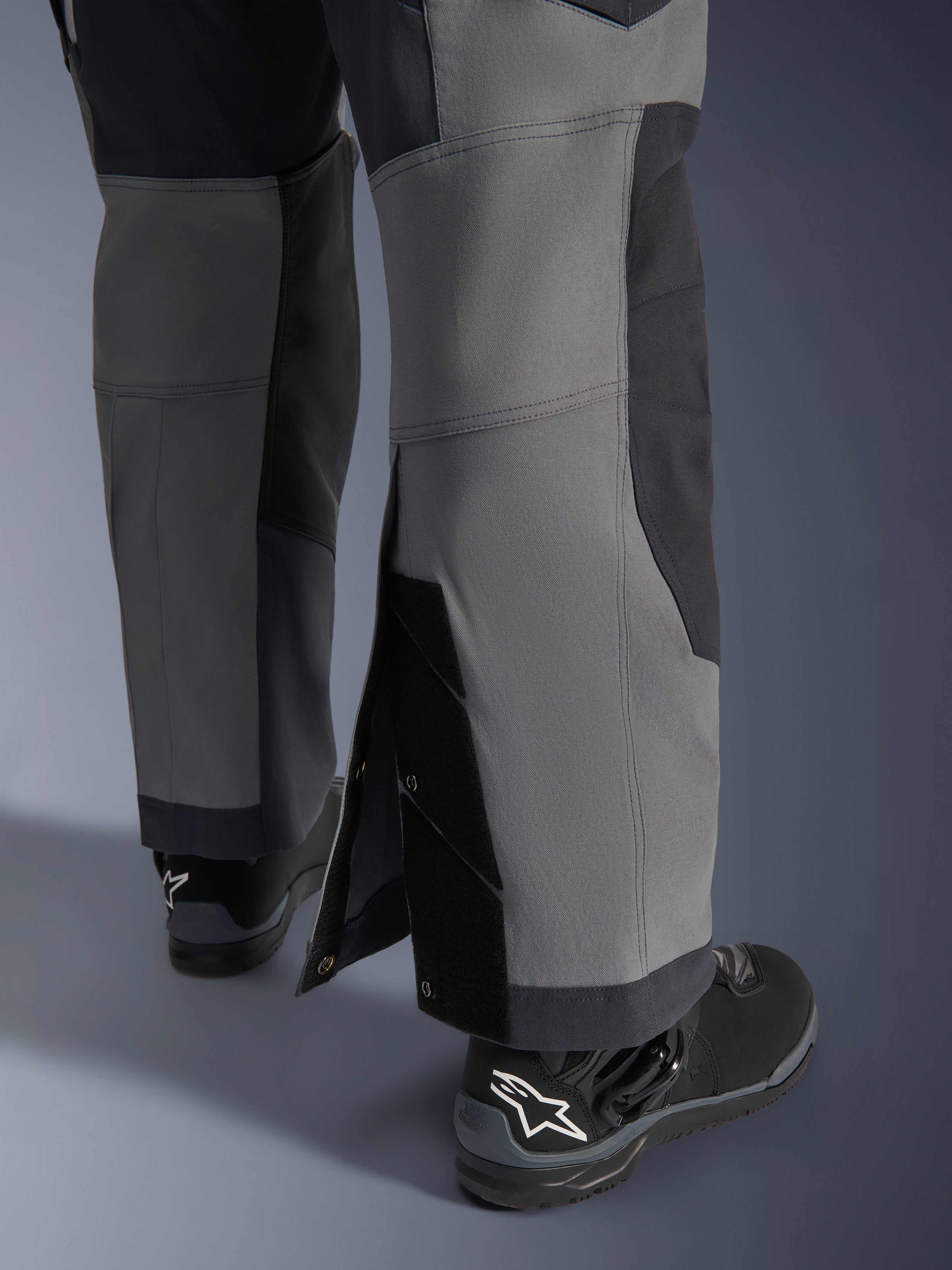 Alpinestars Maxdura Dual Pants, Adventure Motorcycle Pants, Dark Gray and Deep Gray, close-up view of adjustable over-the-boot leg hem with snap closures and reinforced panels, worn with black Alpinestars boots, rugged technical design for dual-sport riding