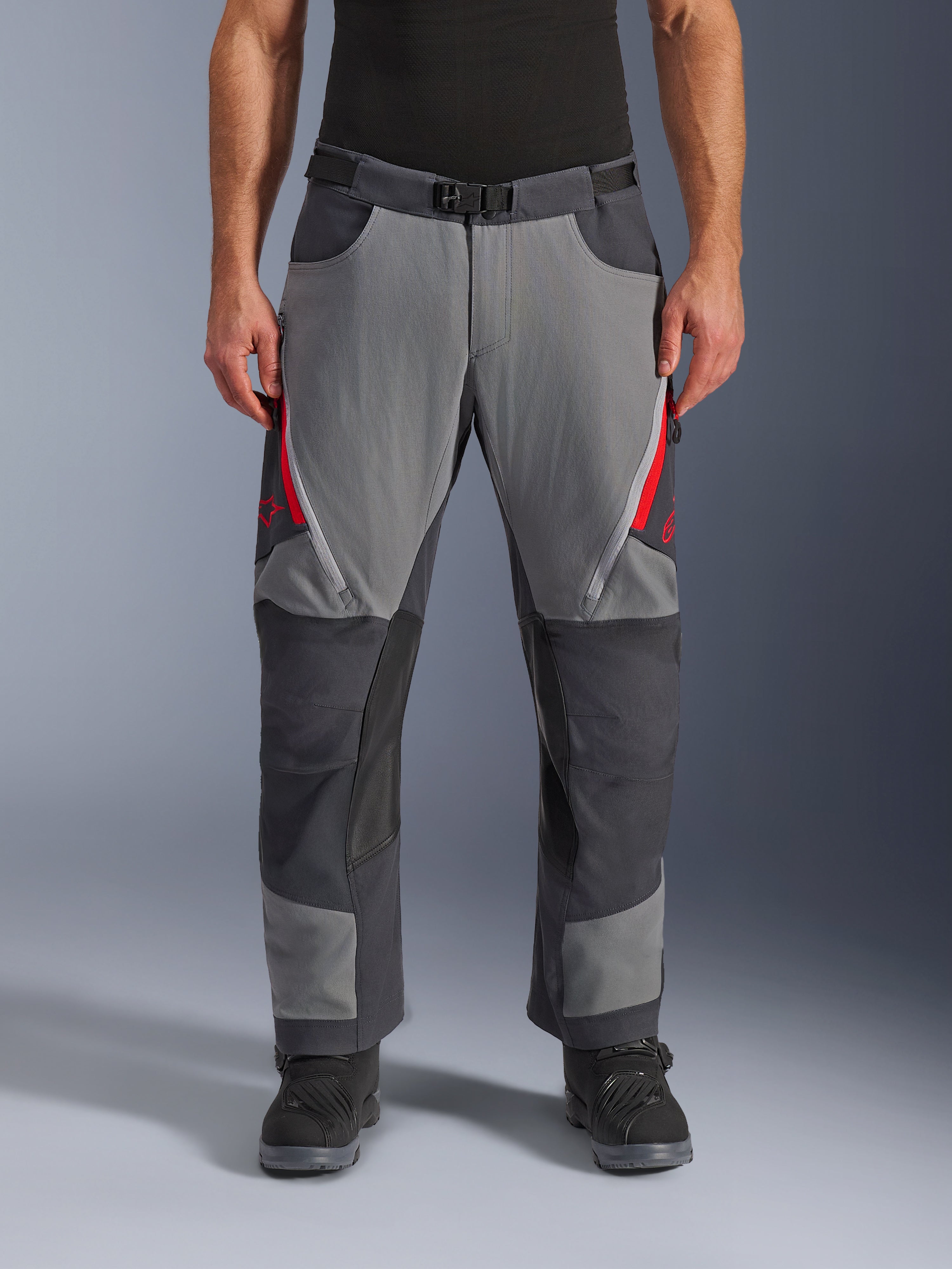 Alpinestars Maxdura Dual Pants, pantalon de moto aventure, gris foncé et gris profond avec des accents rouges, vue de face montrant les aérations zippées aux cuisses, la ceinture à boucle magnétique et les panneaux renforcés aux genoux, conception par-dessus la botte pour le dual-sport.