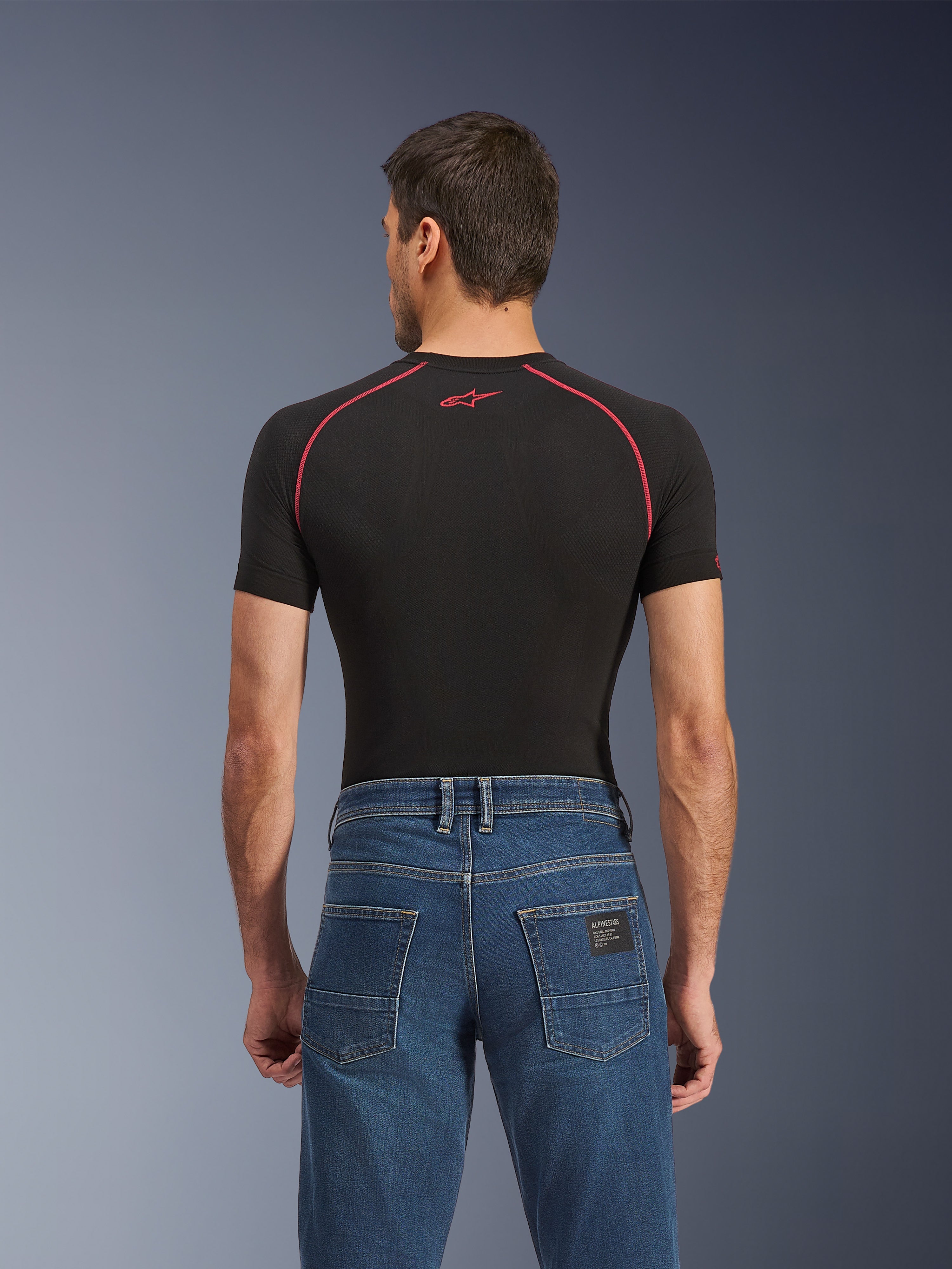 Alpinestars Flex-AST 5 Denim Pants - Short, jean de moto bleu Indigo Washed, vue de dos avec poches arrière et une petite étiquette Alpinestars noire, porté avec un haut de compression noir à coutures rouges, vêtement de moto urbain décontracté.