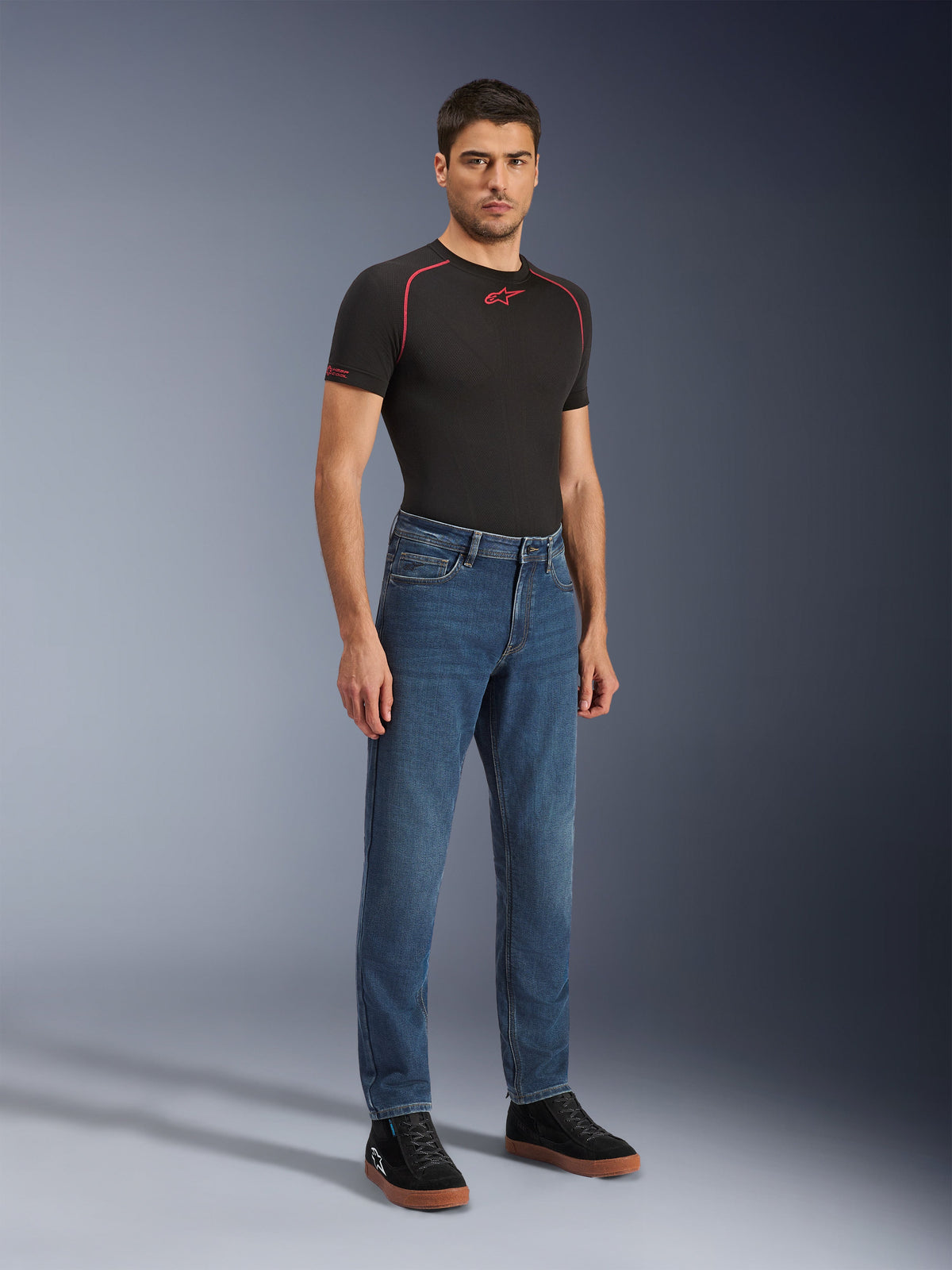 Alpinestars Flex-AST 5 Denim Pants - Short, Indigo Washed, jean de moto urbain avec une coupe fuselée, porté par un mannequin homme avec un t-shirt noir moulant et des baskets noires, style denim classique pour les transitions de la route à la ville