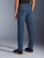 Pantalon Alpinestars Flex-AST 5 Denim, jean de moto urbain pour homme en bleu indigo délavé, vue trois-quarts dos sur mannequin montrant la coupe fuselée, les poches arrière et le style décontracté en denim extensible.