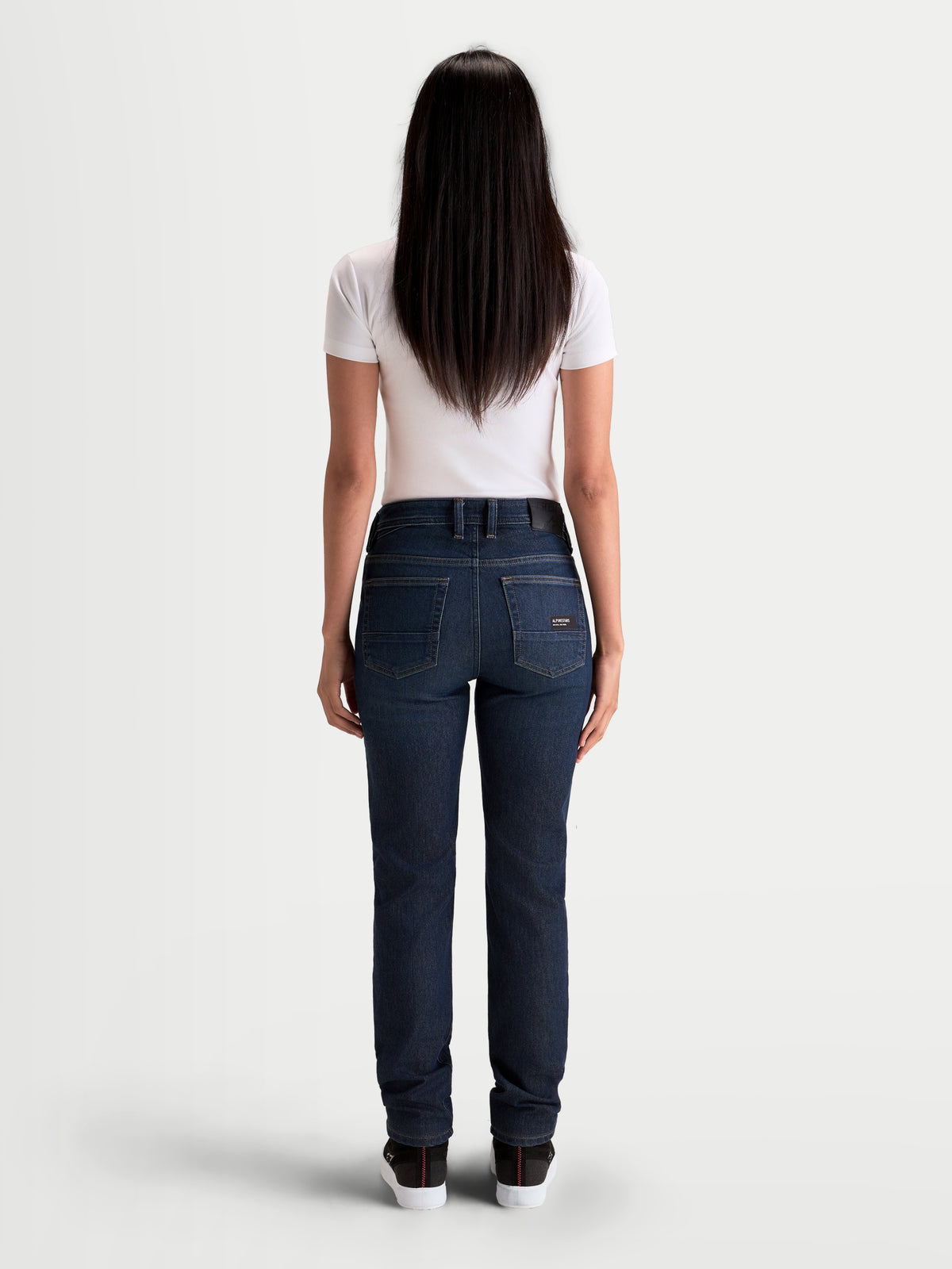 Alpinestars Stella Flex Ast 7 Denim Pantalons, pantalon de moto en denim pour femme en bleu foncé, vue de dos sur un modèle portant un t-shirt blanc, mettant en valeur la construction à cinq poches et l'écusson de dos en cuir