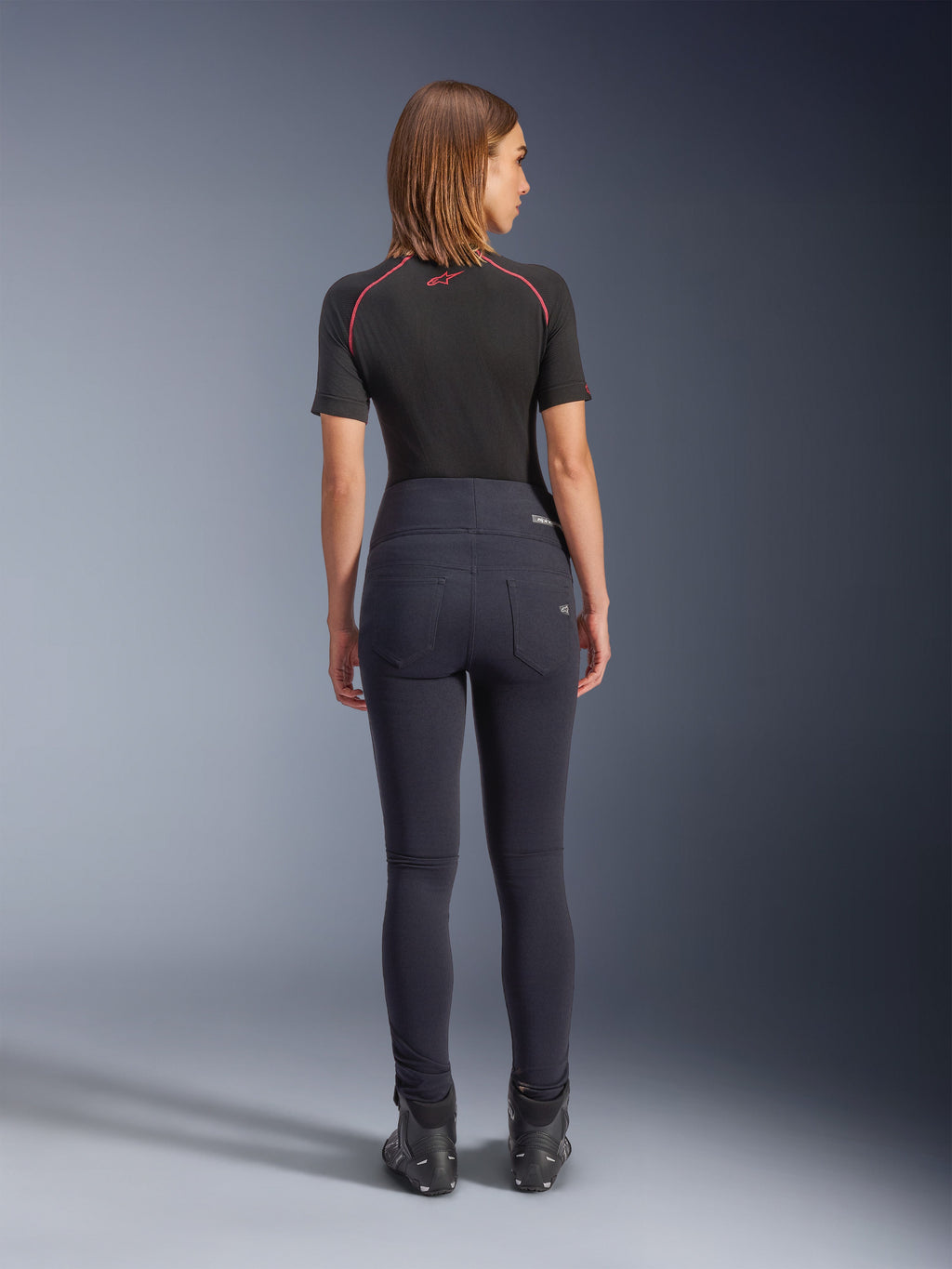 Alpinestars Stella Flex-AST Leggings noir, pantalon de moto taille haute pour femme, vue de dos montrant la coupe skinny et les poches arrière, porté avec un haut noir à manches courtes et des bottes de moto, équipement de conduite urbaine