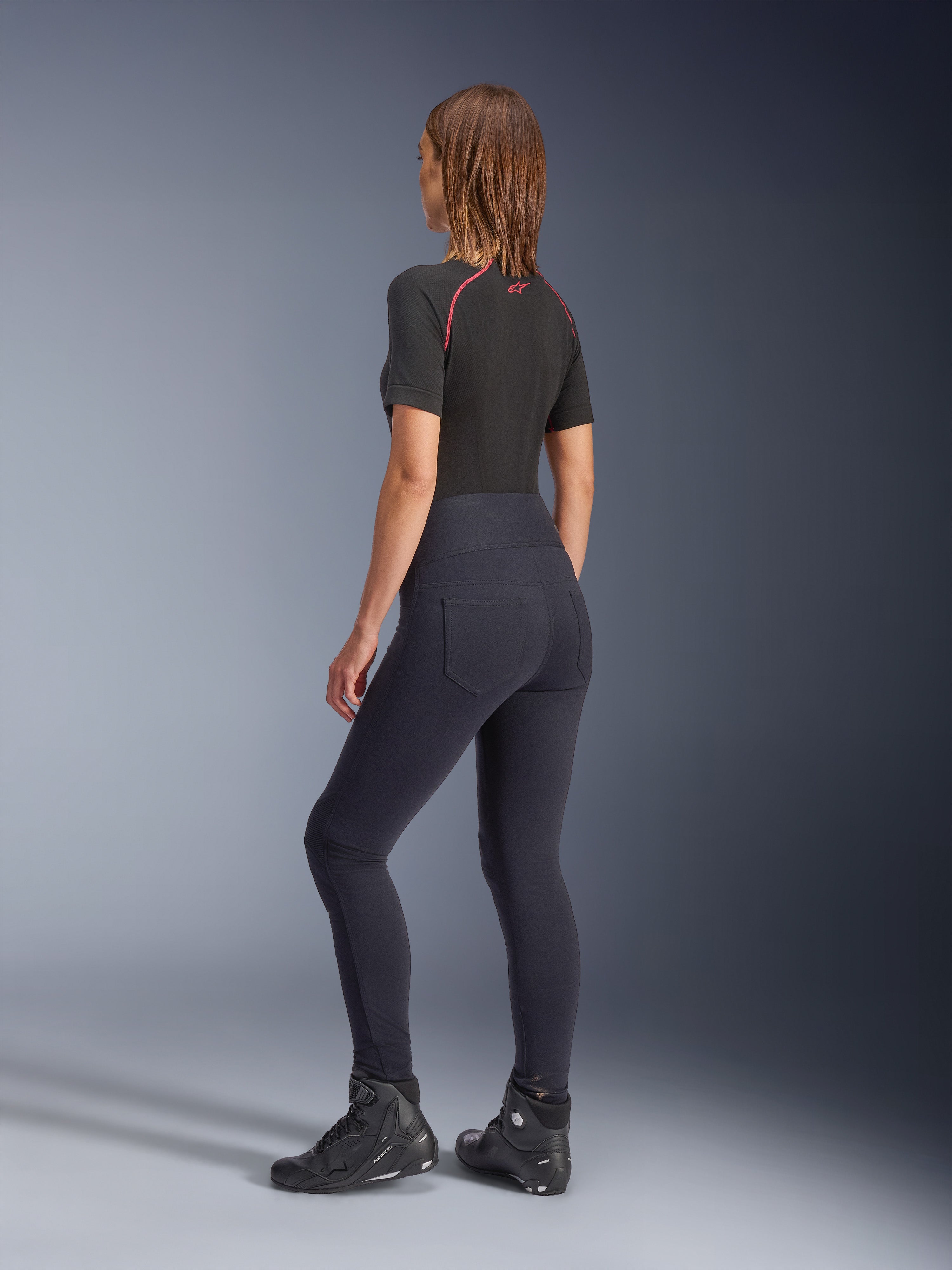 Legging Stella Flex-AST Alpinestars pour femme, legging de moto noir à taille haute, vue de dos montrant la coupe skinny et les poches arrière, porté avec un haut noir à manches courtes et des bottes de moto, tenue de moto urbaine pour femme