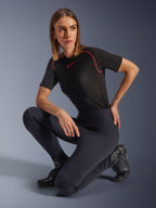 Femme portant les leggings Alpinestars Stella Flex-AST, leggings de moto skinny noirs à taille haute avec panneaux accordéon aux genoux, assortis d'un t-shirt technique noir à manches courtes avec surpiqûres roses et de bottes de moto