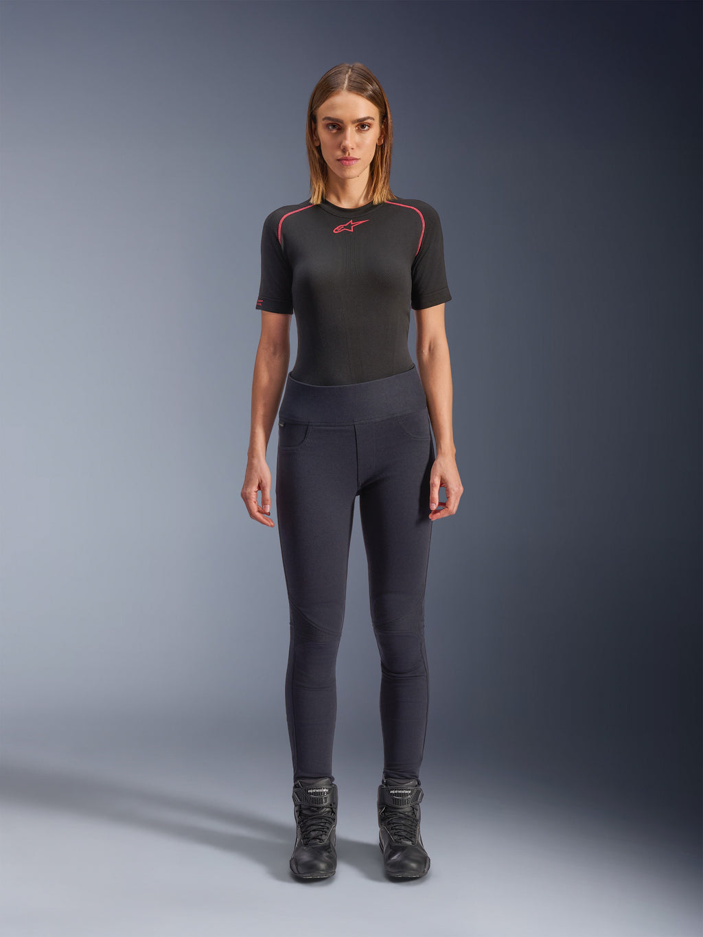 Leggings Stella Flex-AST Alpinestars, leggings de moto urbains pour femme en noir, design skinny taille haute porté avec un haut technique noir à manches courtes et des bottes de moto noires, avec panneaux accordéon aux genoux et un look minimaliste contemporain.