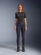 Leggings Stella Flex-AST Alpinestars, leggings de moto urbains pour femme en noir, design skinny taille haute porté avec un haut technique noir à manches courtes et des bottes de moto noires, avec panneaux accordéon aux genoux et un look minimaliste contemporain.