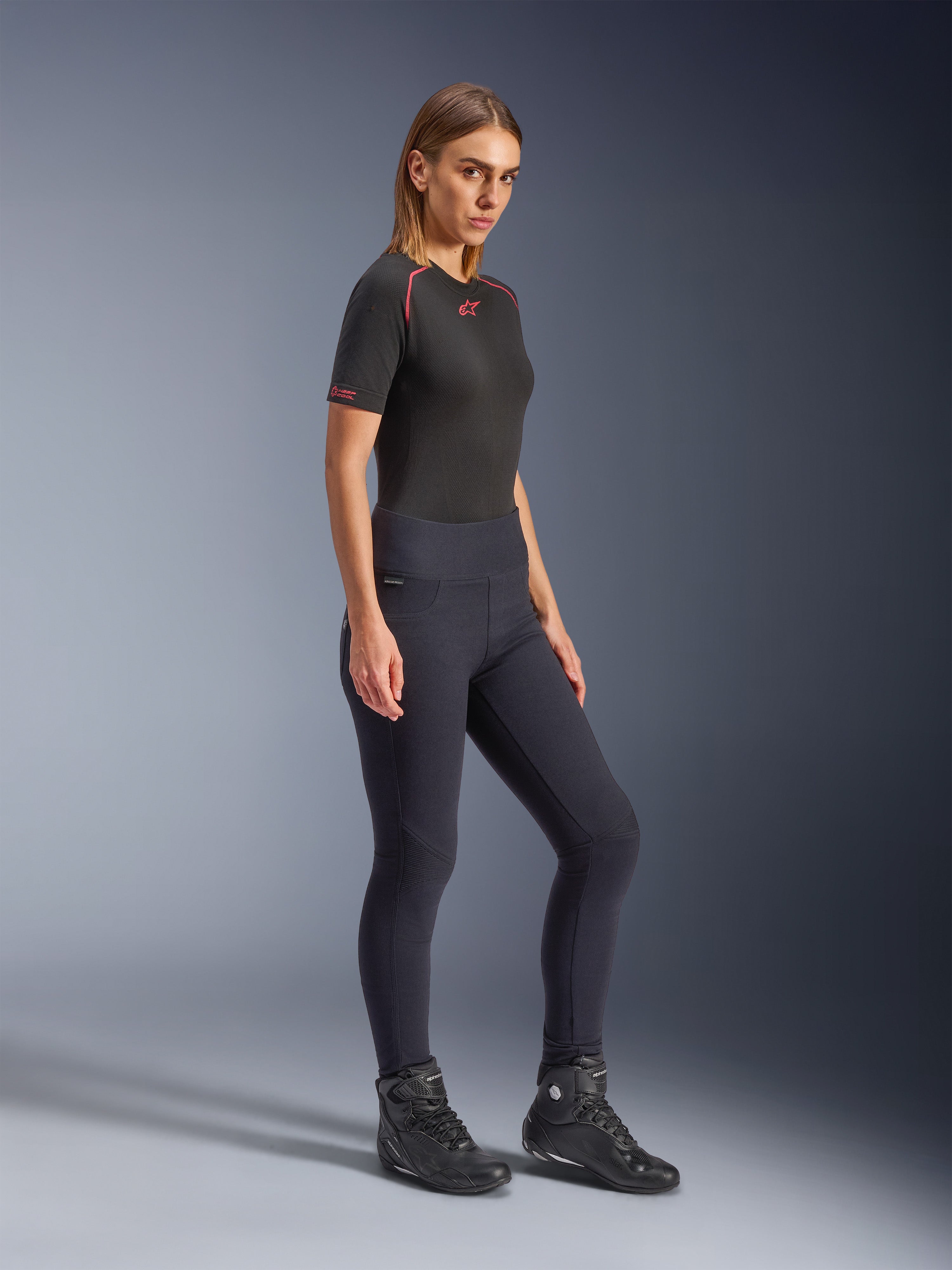 Leggings Alpinestars Stella Flex-Ast, leggings de moto pour femme noirs, design coupe slim à taille haute, portés avec un t-shirt noir aux détails rouges et des bottes de moto noires, prise de vue studio en pied
