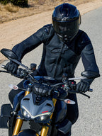 Motorcyclist riding a grey Ducati, wearing the Alpinestars Dusk Leather Jacket in Black, featuring embossed logos and external shoulder protection, paired with a black full-face helmet and riding gloves for a premium road-focused look.
