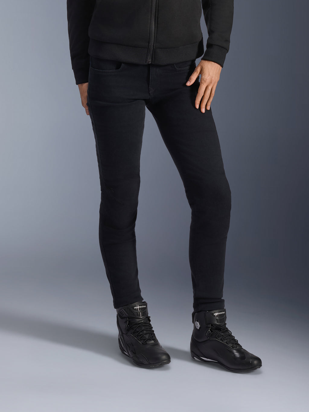 Alpinestars Daisy V3, jean de moto pour femme, noir, coupe ajustée, porté avec des bottines de moto montantes et un sweat à capuche zippé noirs, style urbain monochrome épuré