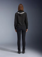 Denim de moto pour femme Daisy V3, Black Rinse, pantalon de moto coupe slim, vue arrière montrant la taille haute et une silhouette féminine, associé à un sweat à capuche Alpinestars noir et des bottes de moto noires, équipement de conduite urbain décontracté