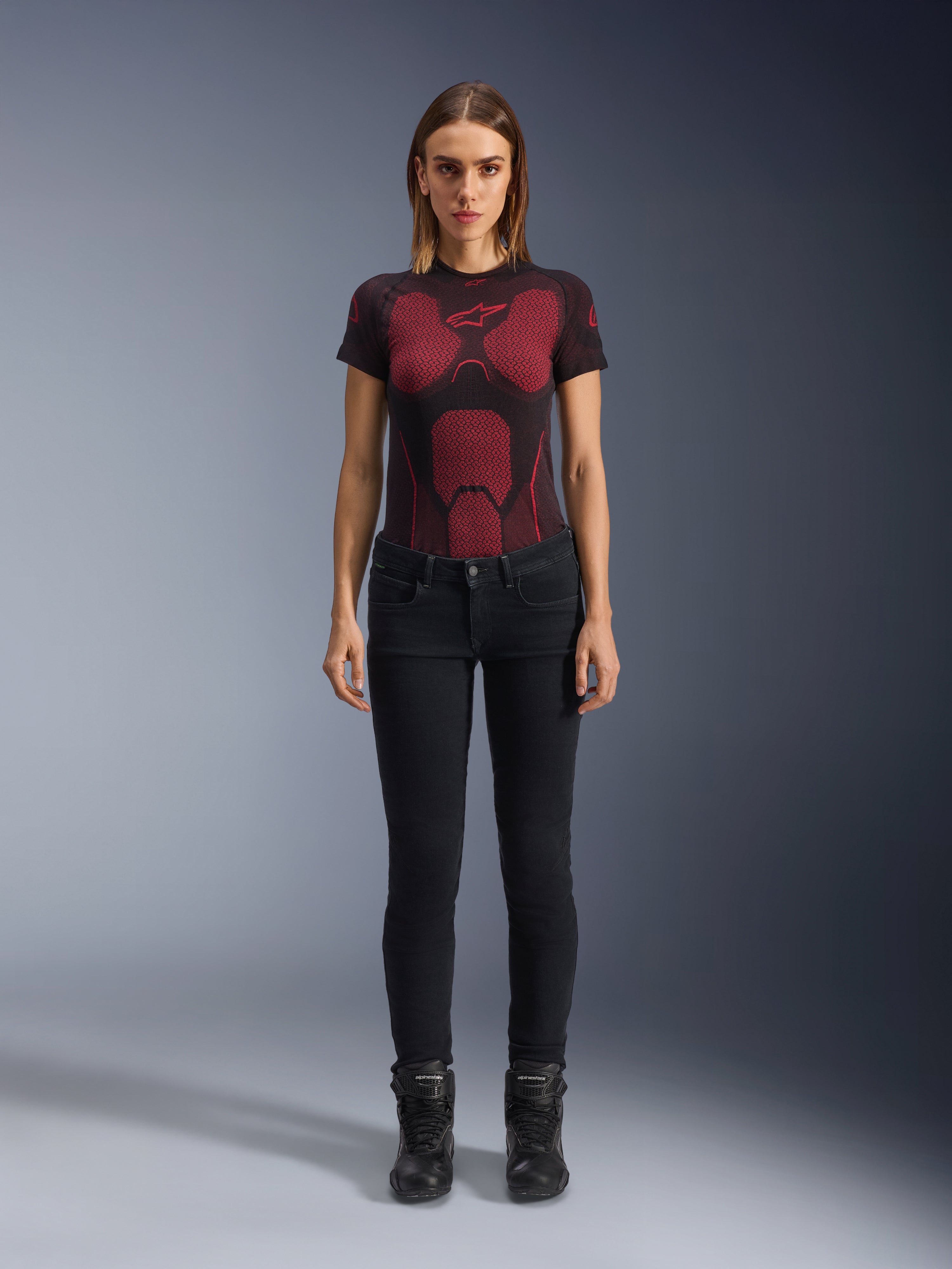 Alpinestars Daisy V3 Women's Riding Denim, Noir, pantalon de moto coupe slim, porté par un mannequin avec un t-shirt technique à motifs rouges et noirs et des bottes de moto noires, équipement urbain décontracté avec une silhouette féminine et une taille haute.