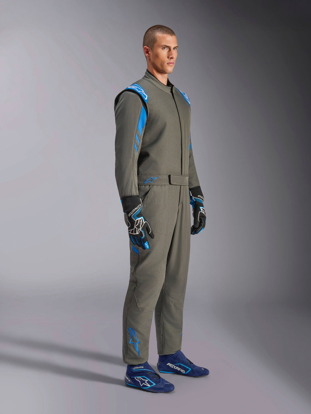 Combinaison Alpinestars GP Race V3 FIA en Anthracite Blue, combinaison de course automobile une pièce portée par un mannequin homme, avec des accents bleu vif sur les épaules et les chevilles, associée à des gants et des chaussures de course bleues assortis, équipement de sport automobile professionnel.