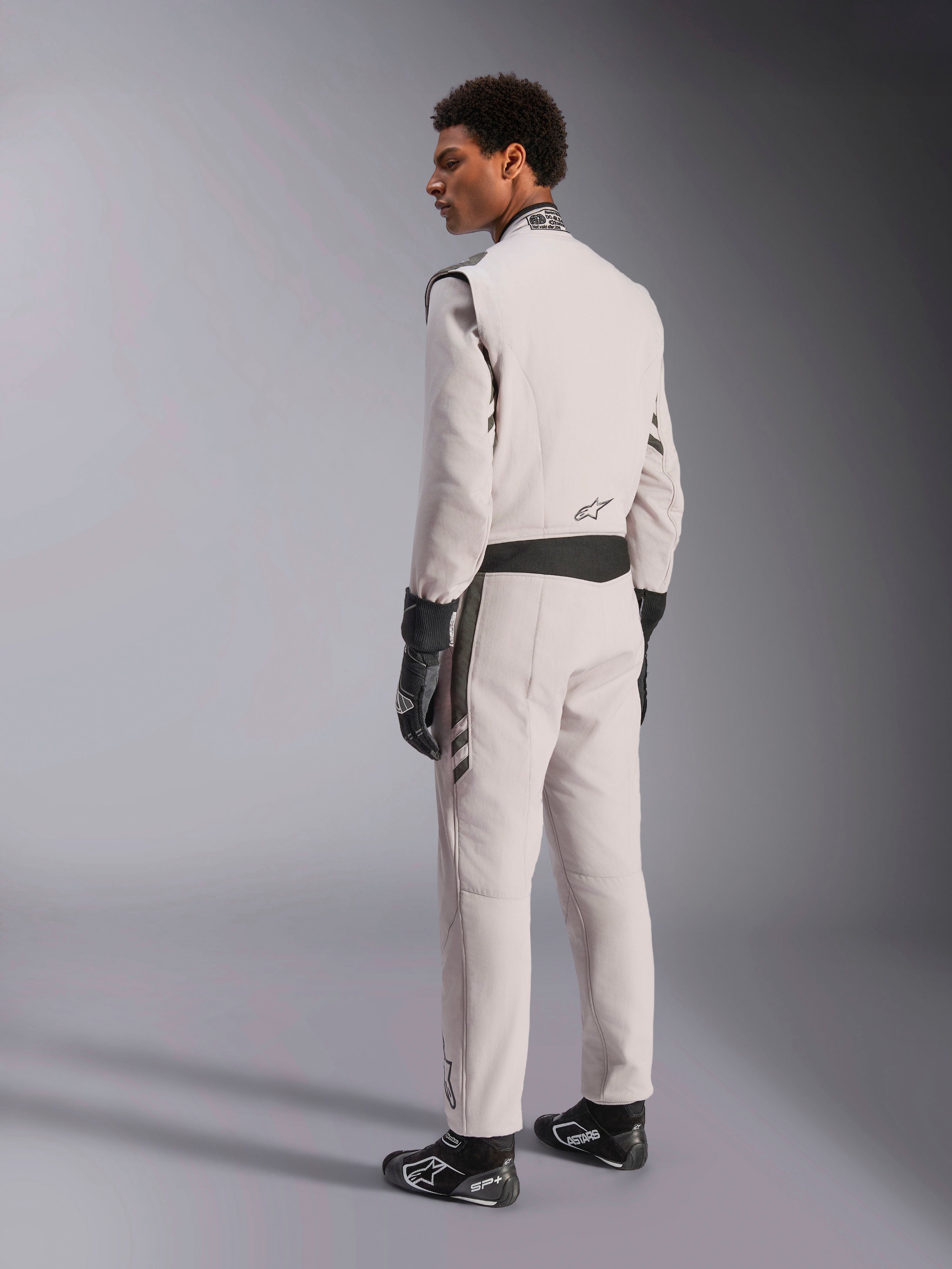 Alpinestars GP Race V3 Suit FIA, combinaison de course Argent Anthracite, vue de profil et de dos, portée avec des gants et des bottines de course noirs, avec des détails gris foncé à la taille et aux épaules, équipement de protection professionnel pour la course automobile.