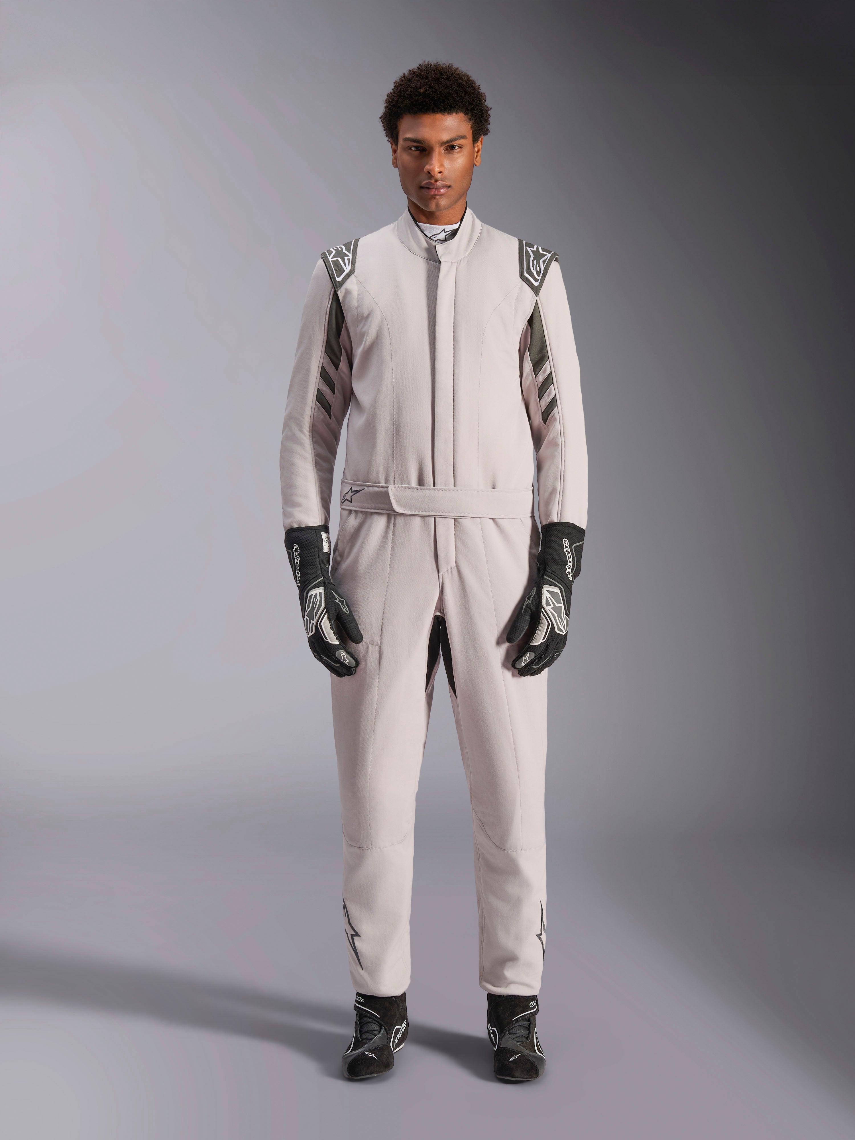Alpinestars GP Race V3 Suit FIA en Silver Anthracite, combinaison de course automobile une pièce portée par un mannequin, dotée d'épaulettes et de détails gris foncé, accompagnée de gants et de bottines de course noirs, équipement de protection professionnel pour le sport automobile