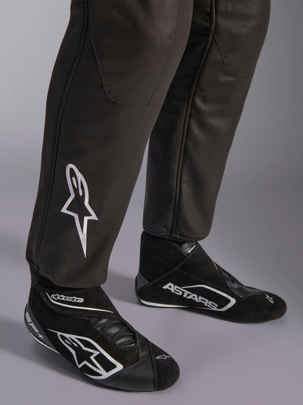 Combinaison Alpinestars GP Race V3 FIA, gros plan sur le bas des jambes et les bottines de course, noir avec accents argentés, arborant un logo étoile blanc brodé sur le tibia et des poignets de cheville côtelés, équipement de protection professionnel pour la course automobile
