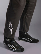 Combinaison Alpinestars GP Race V3 FIA, gros plan sur le bas des jambes et les bottines de course, noir avec accents argentés, arborant un logo étoile blanc brodé sur le tibia et des poignets de cheville côtelés, équipement de protection professionnel pour la course automobile