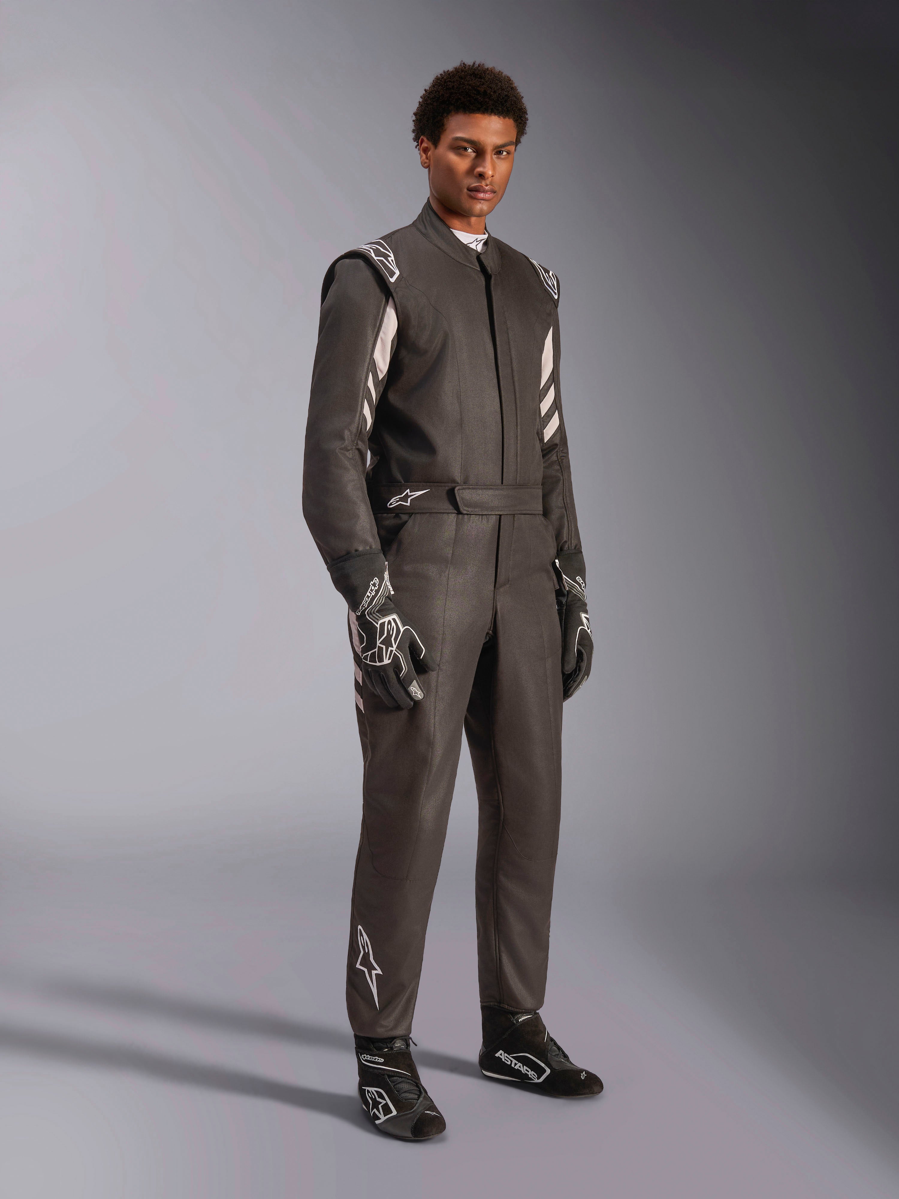 Pilote portant une combinaison Alpinestars GP Race V3 FIA, combinaison de course automobile noir et argent, avec gants et chaussures assortis, détails argentés sur les épaules et le bas des jambes, équipement de course automobile professionnel avec coupe ajustée