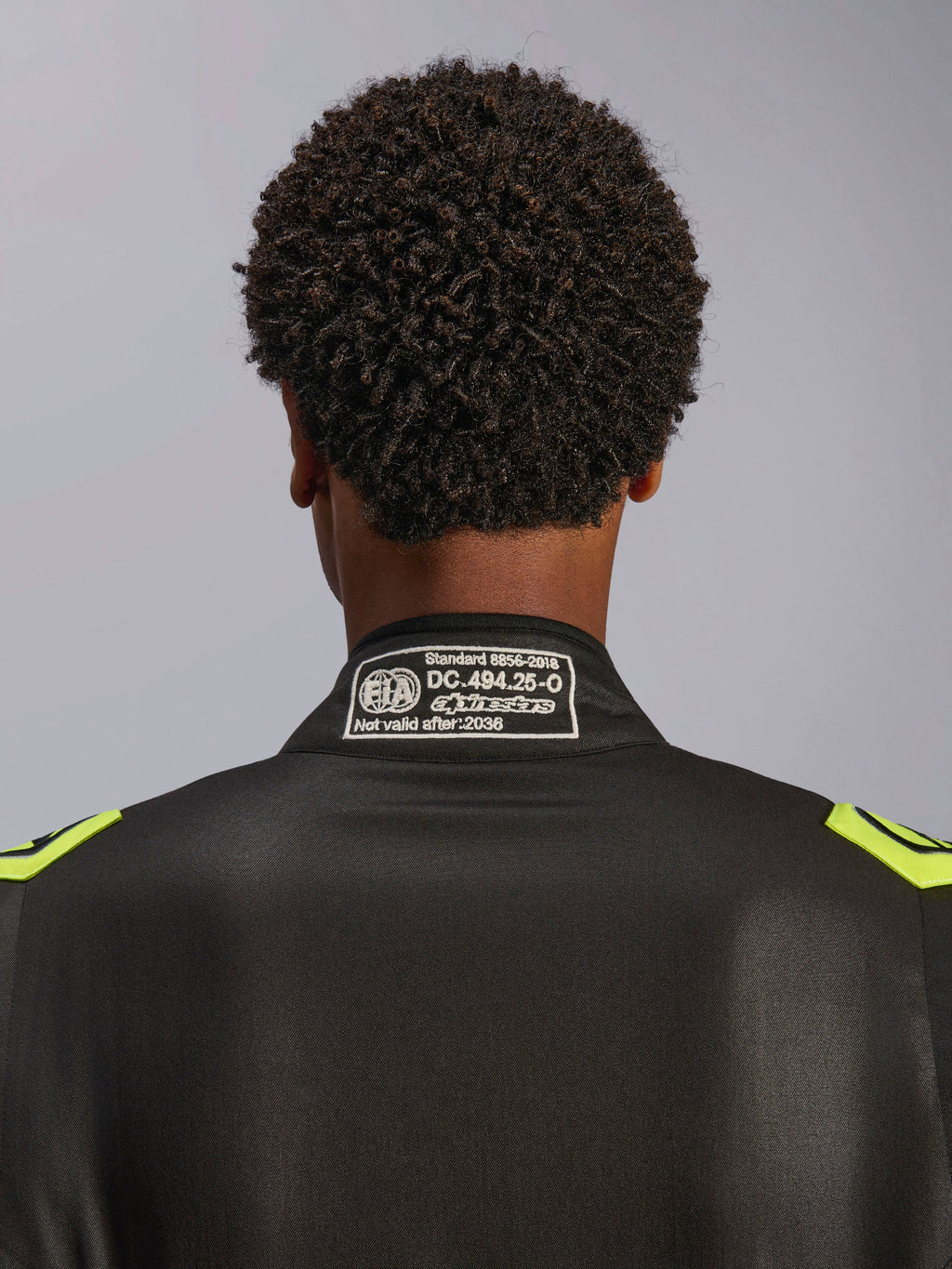 Alpinestars GP Race V3 Suit FIA, Black and Yellow Fluo, close-up of the back collar showing the FIA 8856-2018 certification label, professional automotive racing suit.