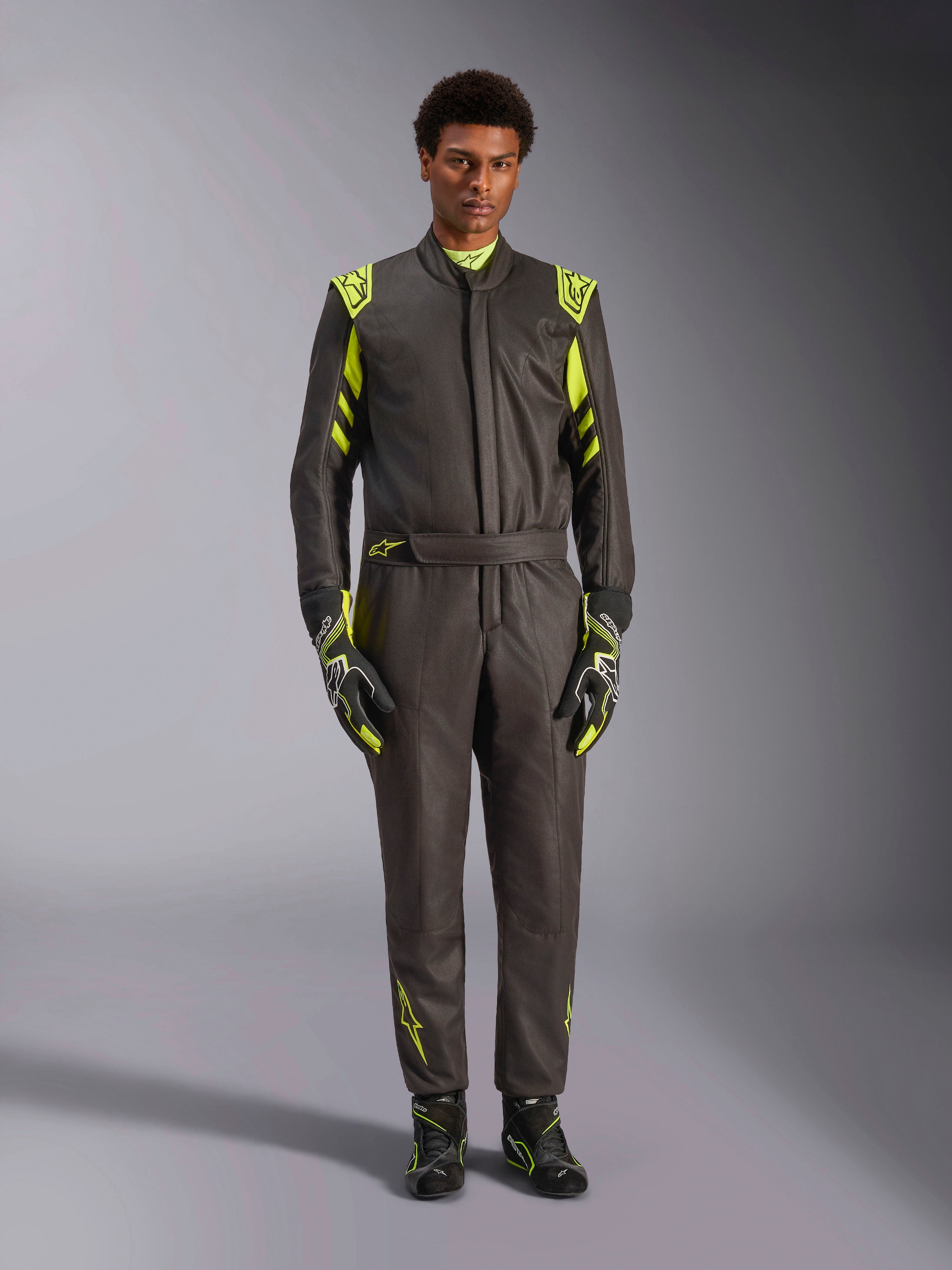 Combinaison Alpinestars GP Race V3 FIA, combinaison de course automobile, noir et jaune fluo, portée par un mannequin avec gants et bottines de course assortis, présentant des accents jaune vif sur les épaules, la taille et les manches, équipement professionnel de sport automobile