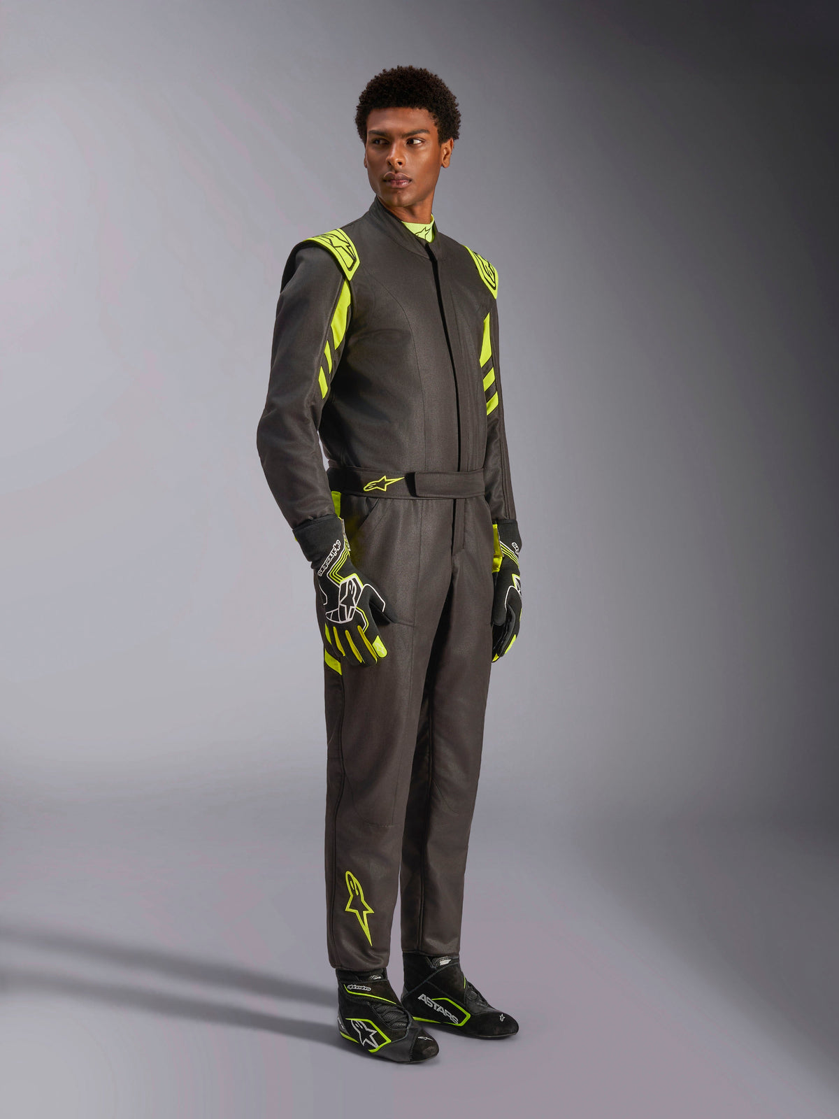 Alpinestars GP Race V3 Suit FIA, combinaison de course automobile, noir et jaune fluo, portée par un mannequin avec des gants et des bottines de course assortis, dotée de touches jaune vif sur les épaules et les jambes, équipement de sport automobile professionnel
